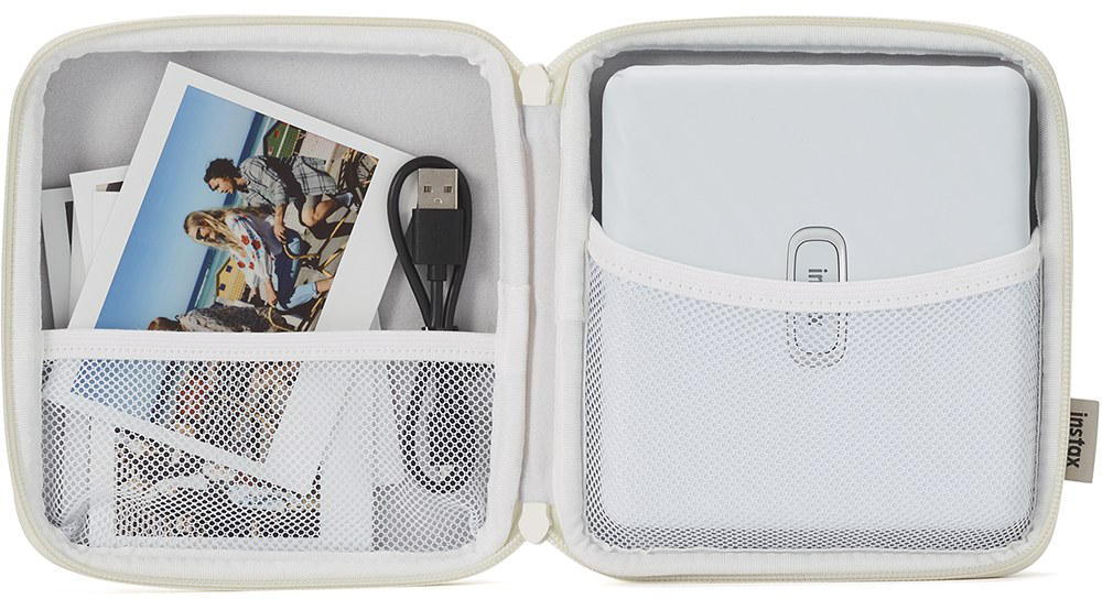 Nyitott fehér Instax tok fotókkal, USB kábellel és fehér nyomtatóval.