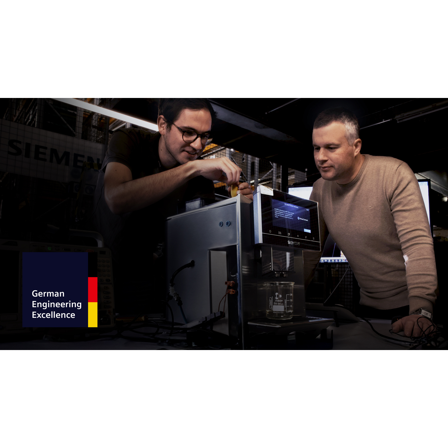Deux hommes travaillent sur une machine de marque Siemens. Un homme avec des lunettes regarde la machine.