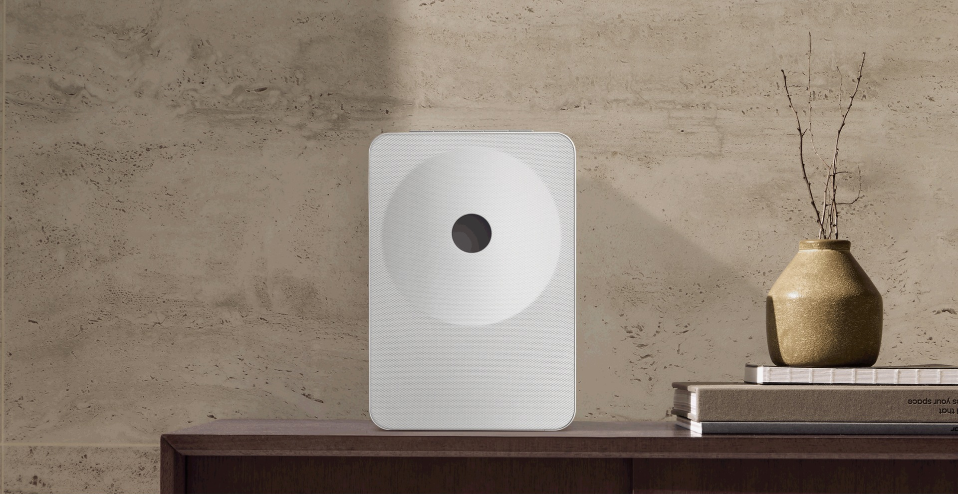 Un haut-parleur blanc avec cercle noir sur table en bois devant mur de pierre.