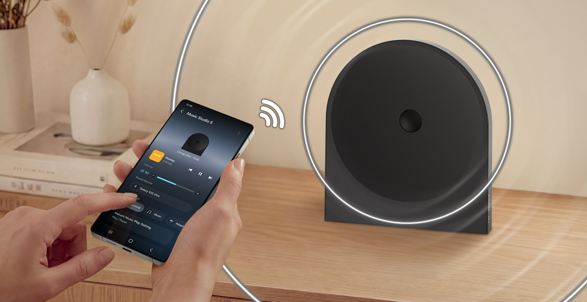 Eine Hand hält ein Smartphone mit Musiksteuerung. Ein schwarzer Lautsprecher steht daneben.
