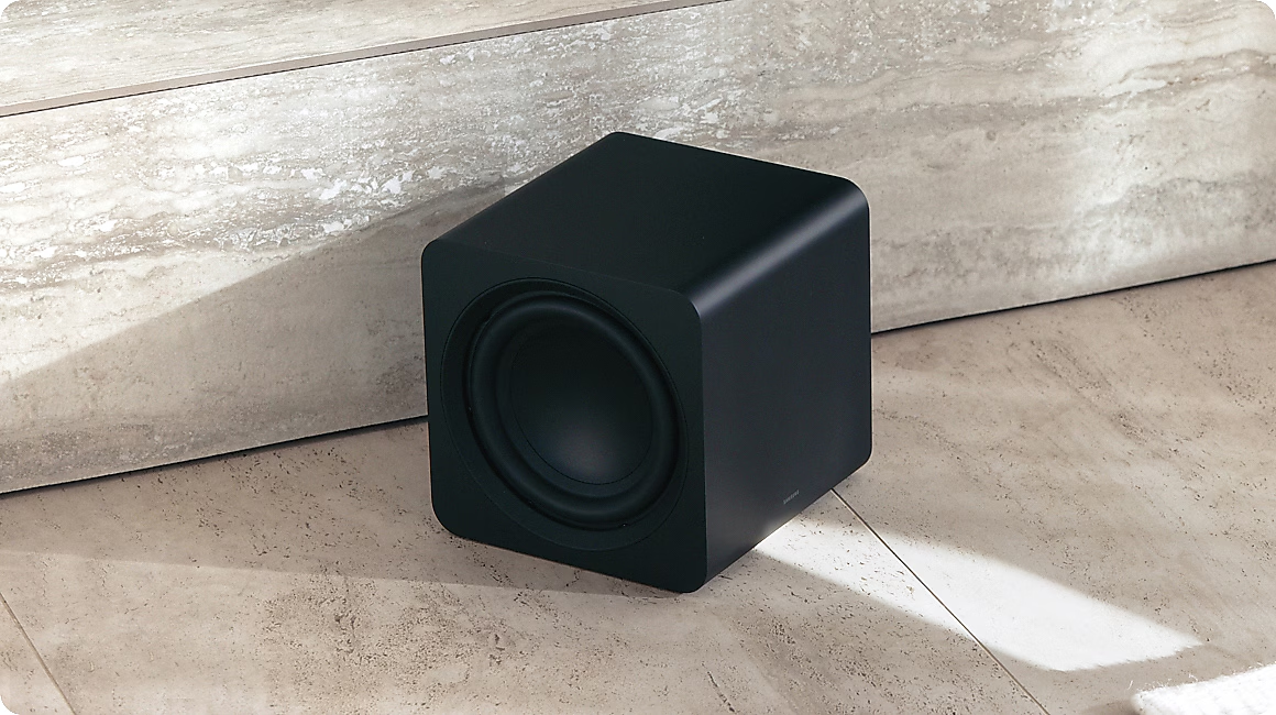 Ein schwarzer Subwoofer mit Bassreflexöffnung steht auf einem hellen Boden.