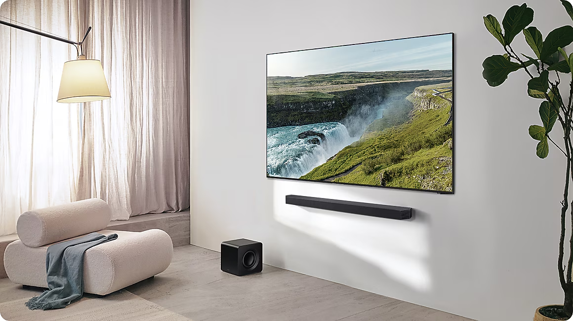 Ein helles Wohnzimmer mit einem Fernseher, der einen Wasserfall zeigt, einer Couch und einem Subwoofer.