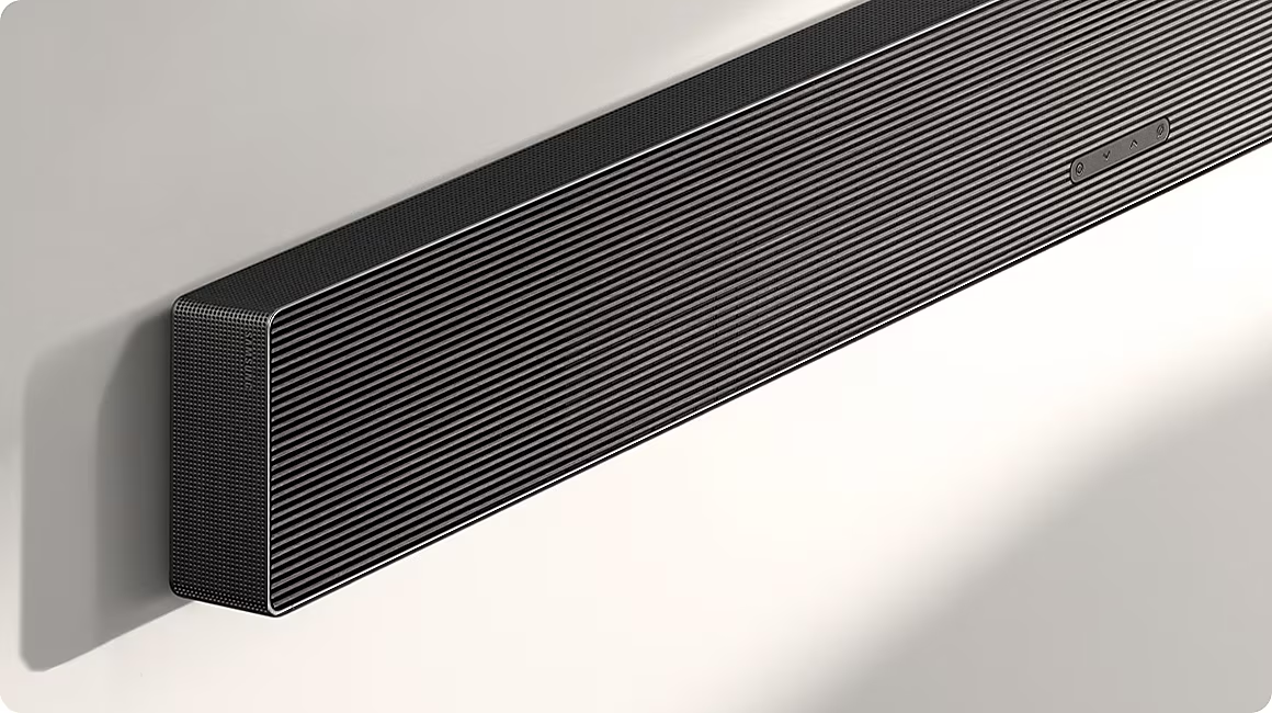Barre de son noire avec grille côtelée et boutons, montée sur un mur.