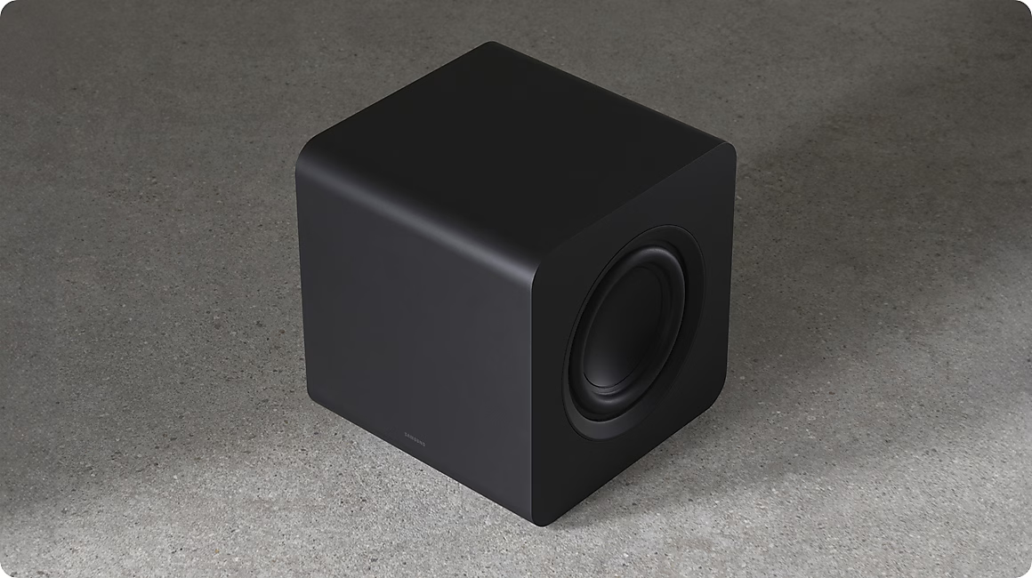 Un subwoofer noir cubique repose sur un sol en béton.