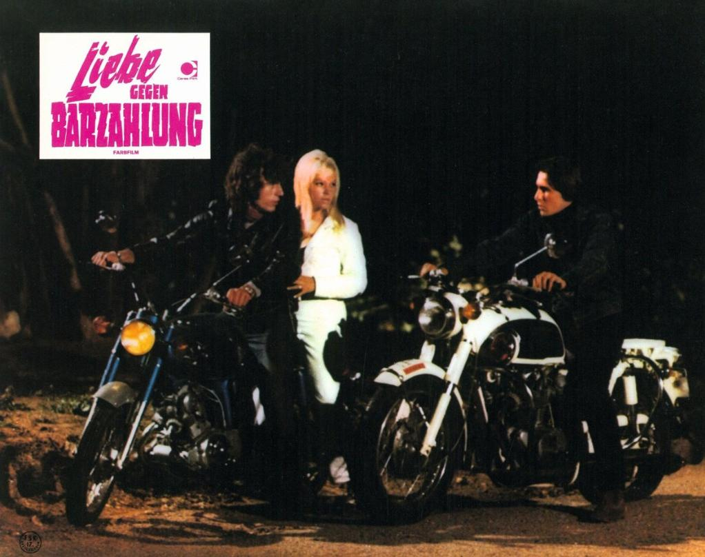 Drei Personen auf Motorrädern bei Nacht. Ein Mann und eine Frau stehen neben einem Motorrad.