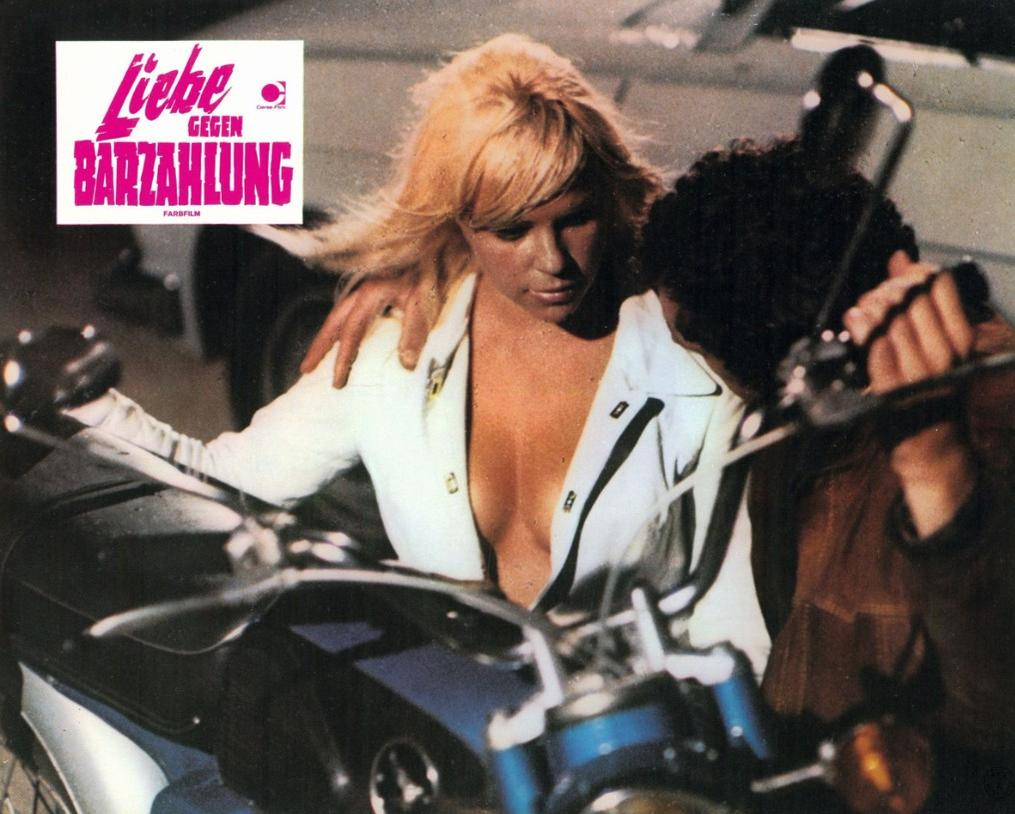 Mann und Frau auf einem Motorrad, Frau trägt weiße Jacke, Mann hält sie.