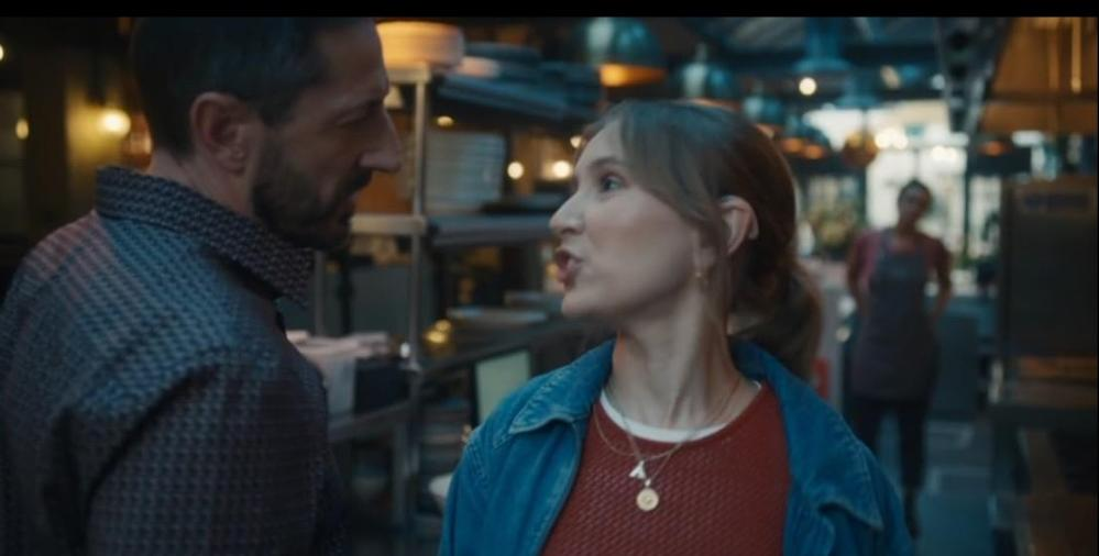 Ein Mann und eine Frau sprechen sich in einem Restaurant. Eine Kellnerin steht im Hintergrund.