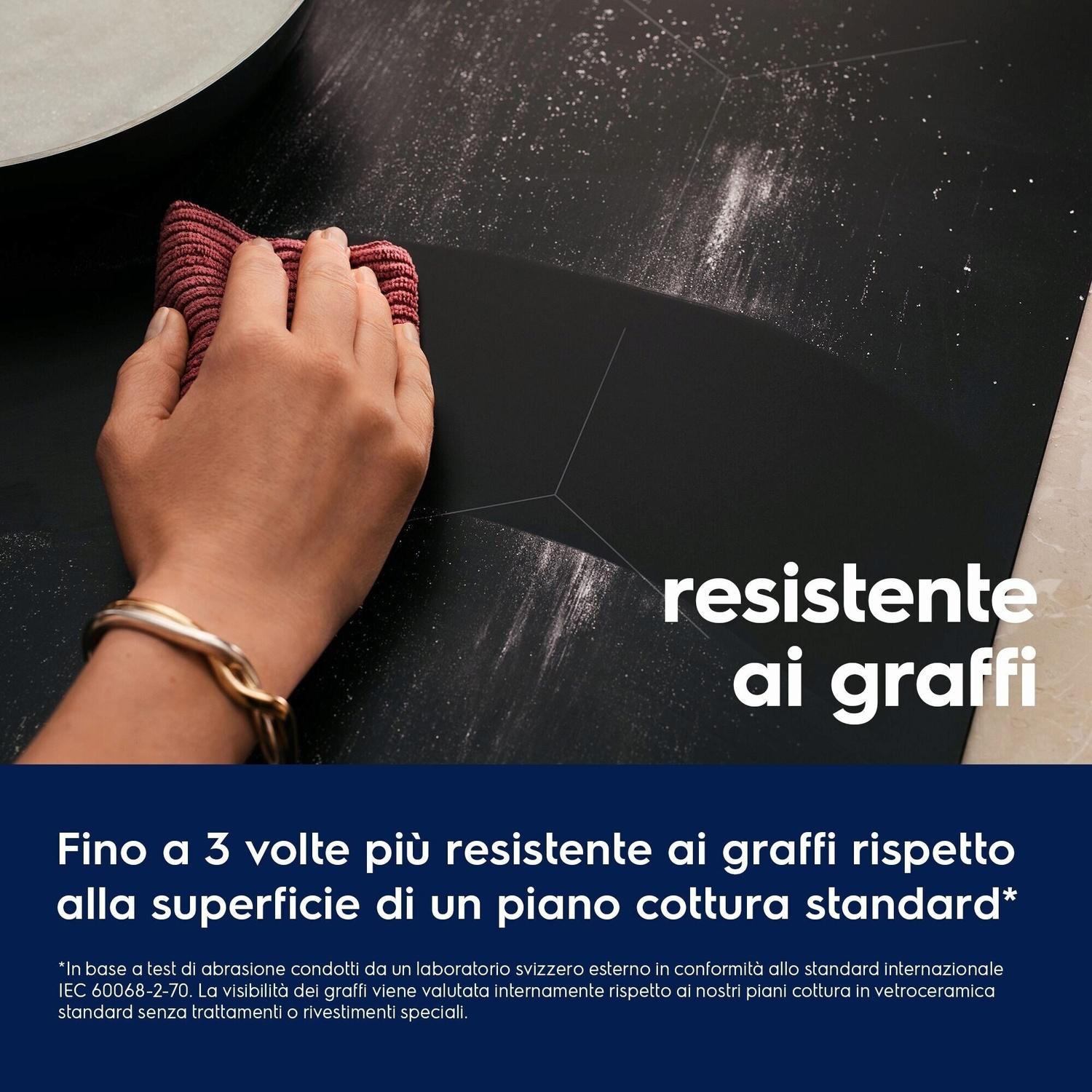 Una mano con un panno rosso pulisce una superficie di piano cottura nera.