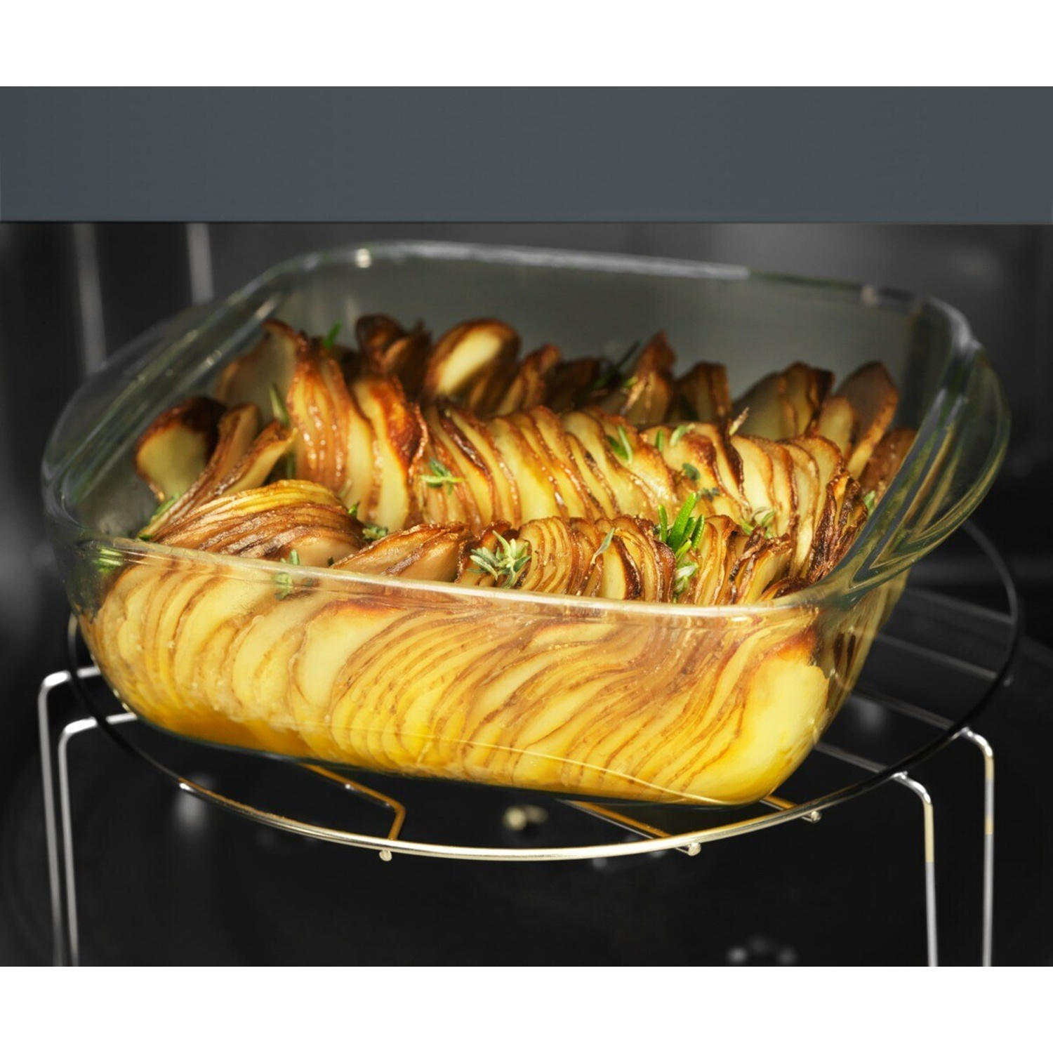 Patate al forno con erbe in una teglia di vetro su una griglia.