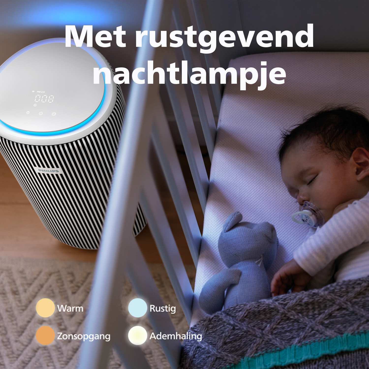Een baby slaapt in een wieg naast een luchtreiniger en een knuffelbeer.