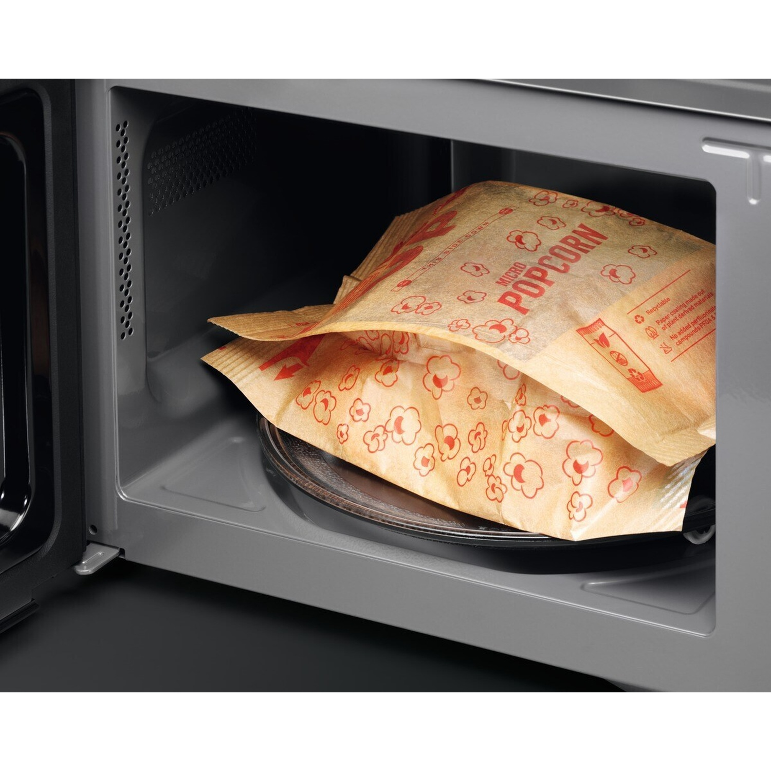 Sacchetto di popcorn per microonde su un piatto girevole di vetro all'interno di un forno a microonde aperto.