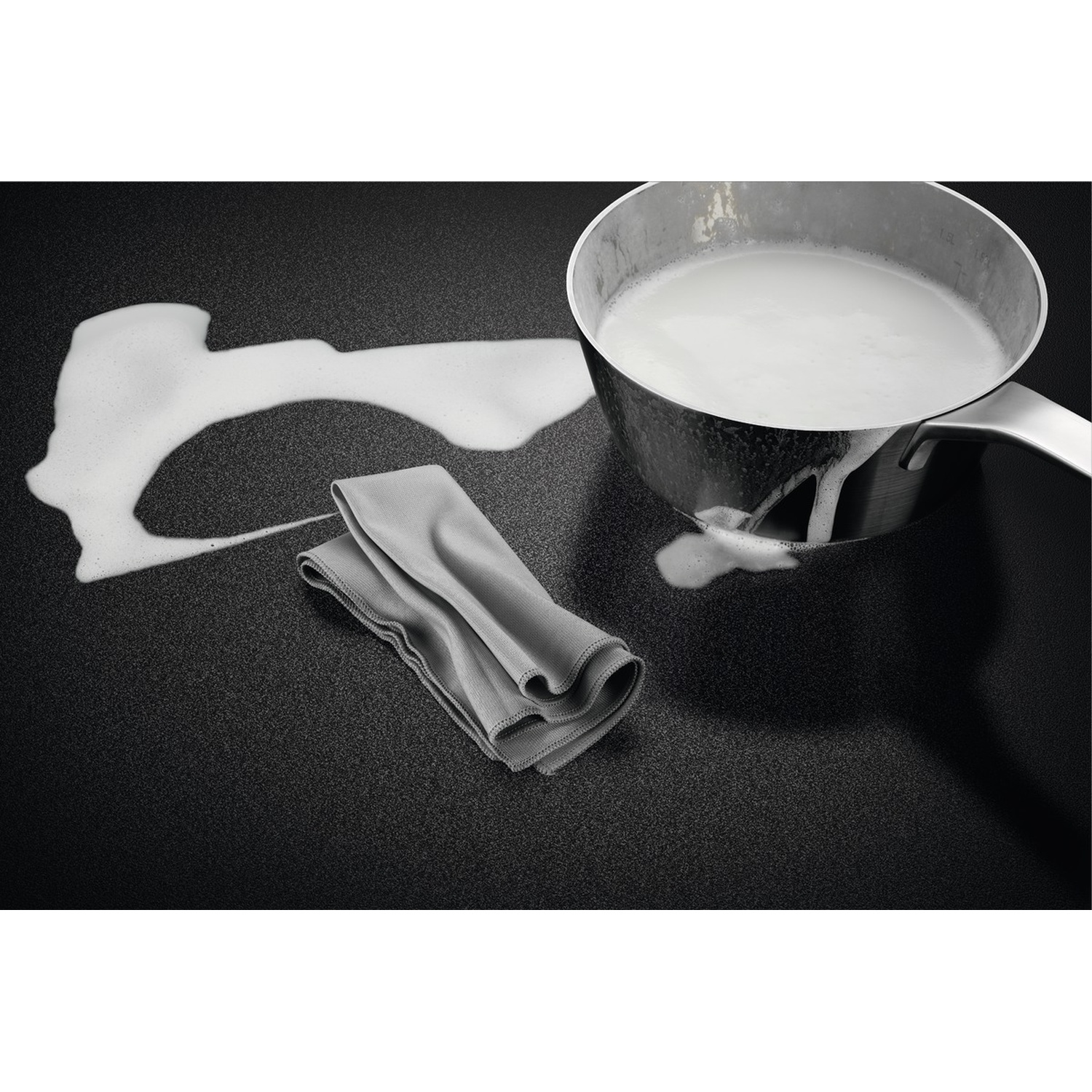 Una pentola di liquido bianco e un panno grigio su una superficie nera.
