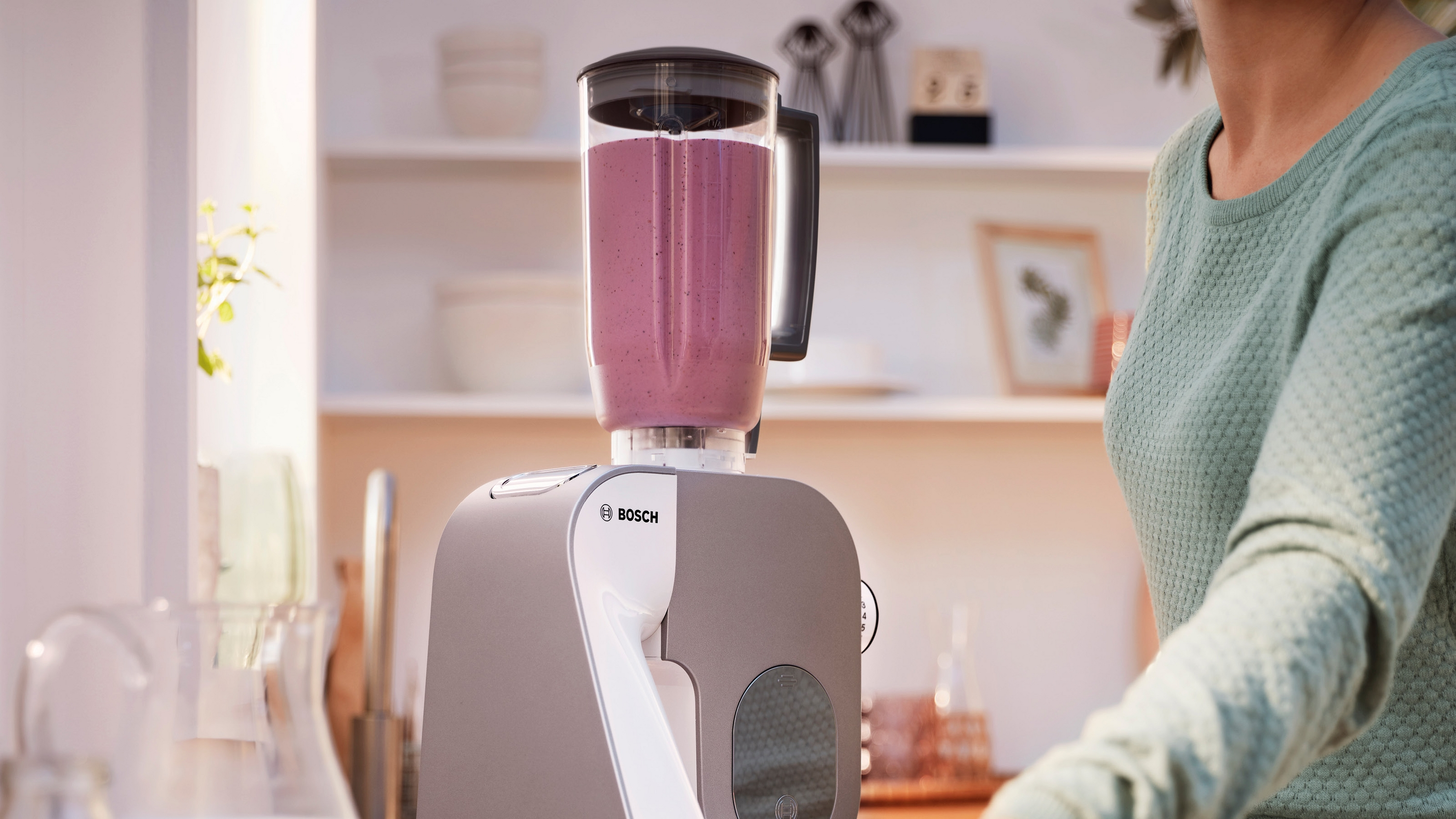 Ein Bosch-Standmixer mit pinkem Smoothie und einer Person im Hintergrund in einer Küche.