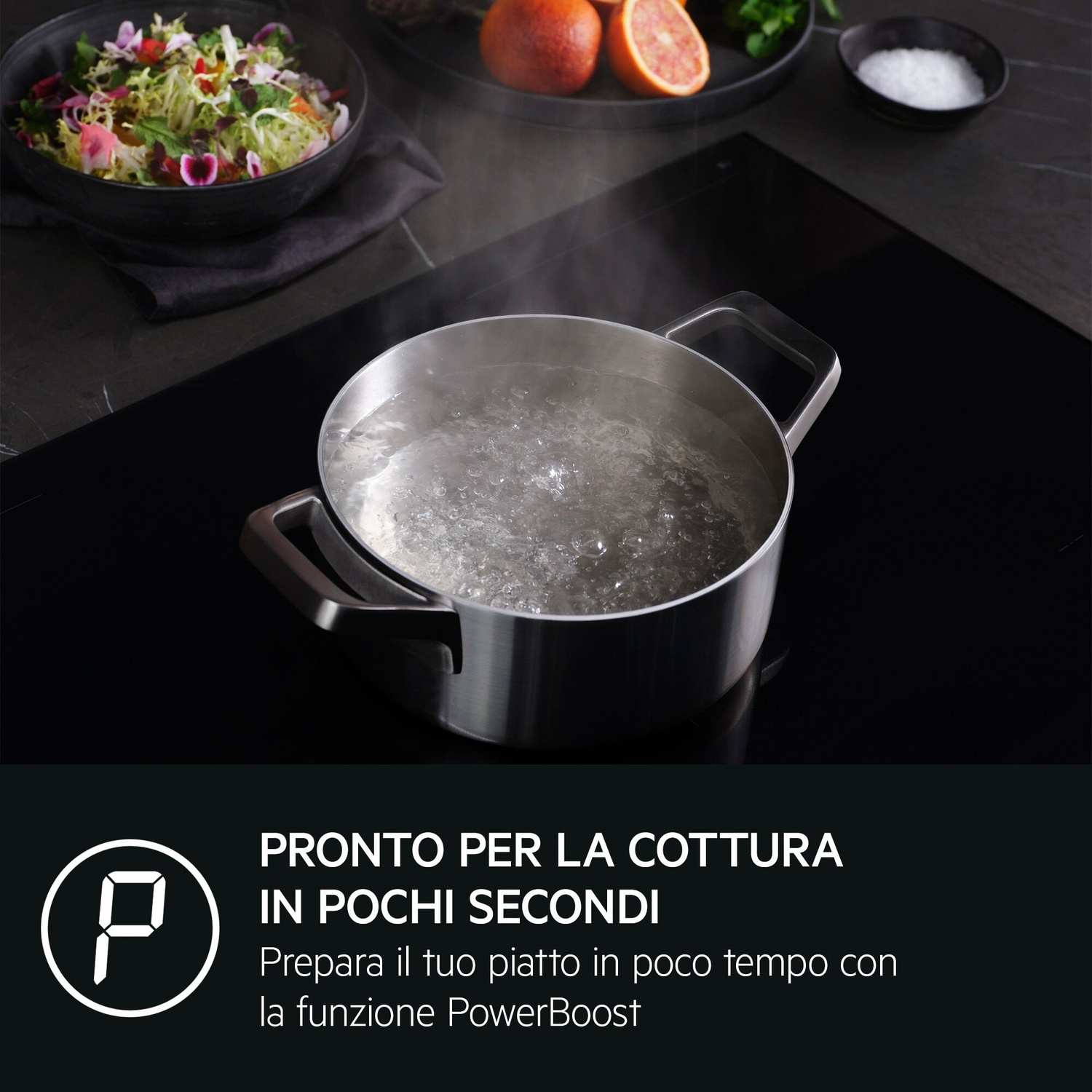 Una pentola di acqua bollente su un piano cottura a induzione, con un'insalata vicina.