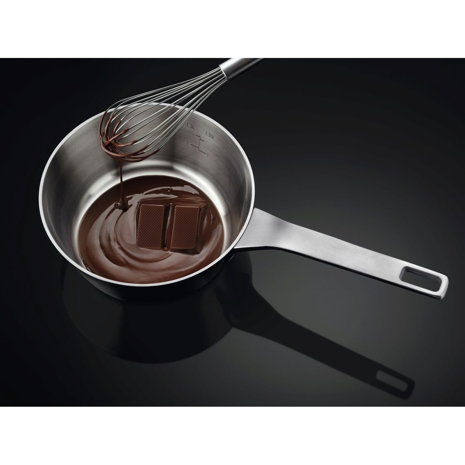 Una frusta fa gocciolare cioccolato fuso in una pentola con pezzi di cioccolato.