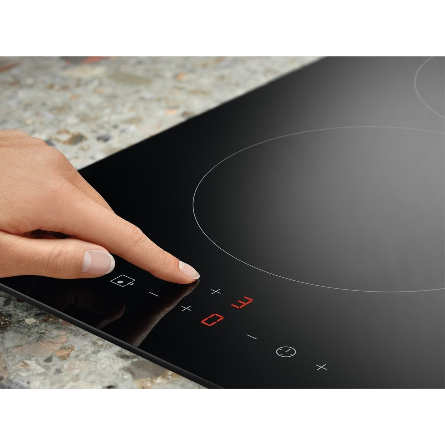 Una mano aziona un piano cottura a induzione nero con controlli digitali rossi.