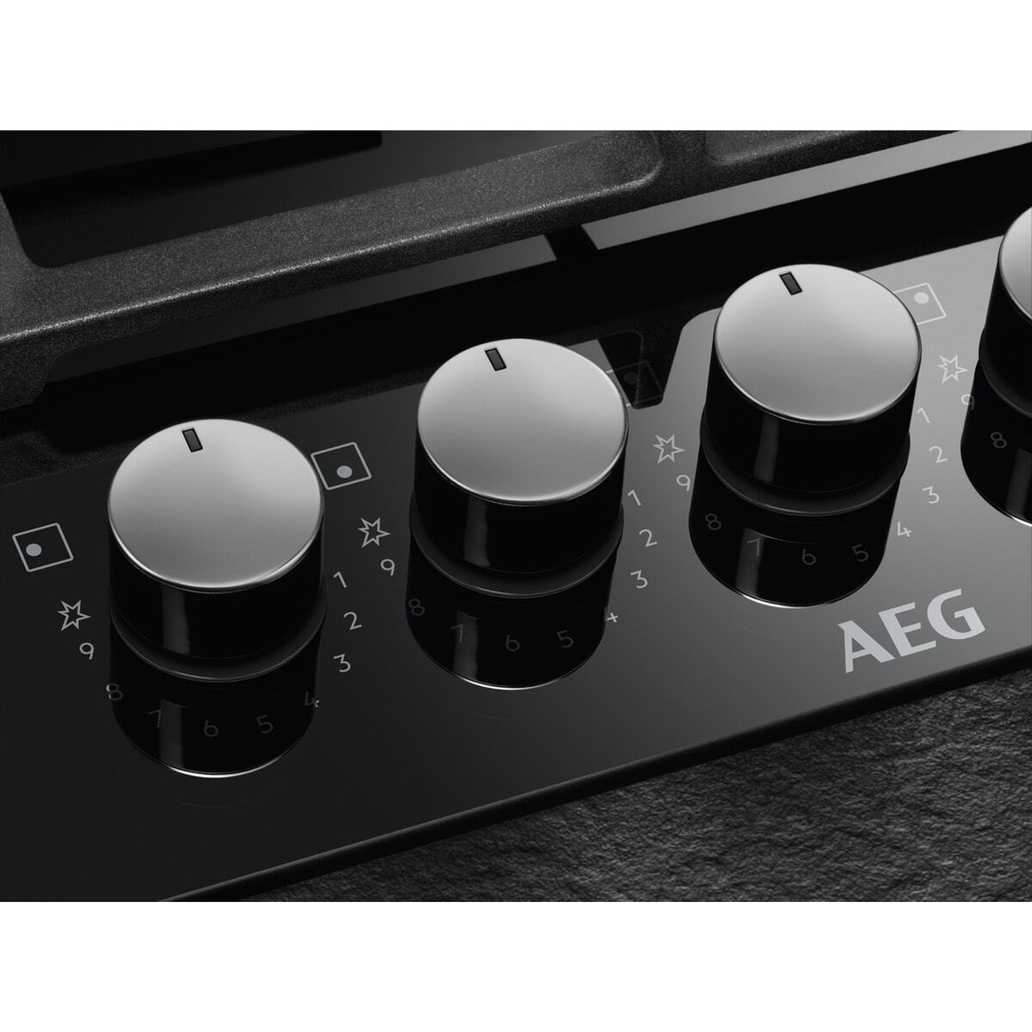 Primo piano di un piano cottura AEG in vetroceramica nero con quattro manopole argentate.