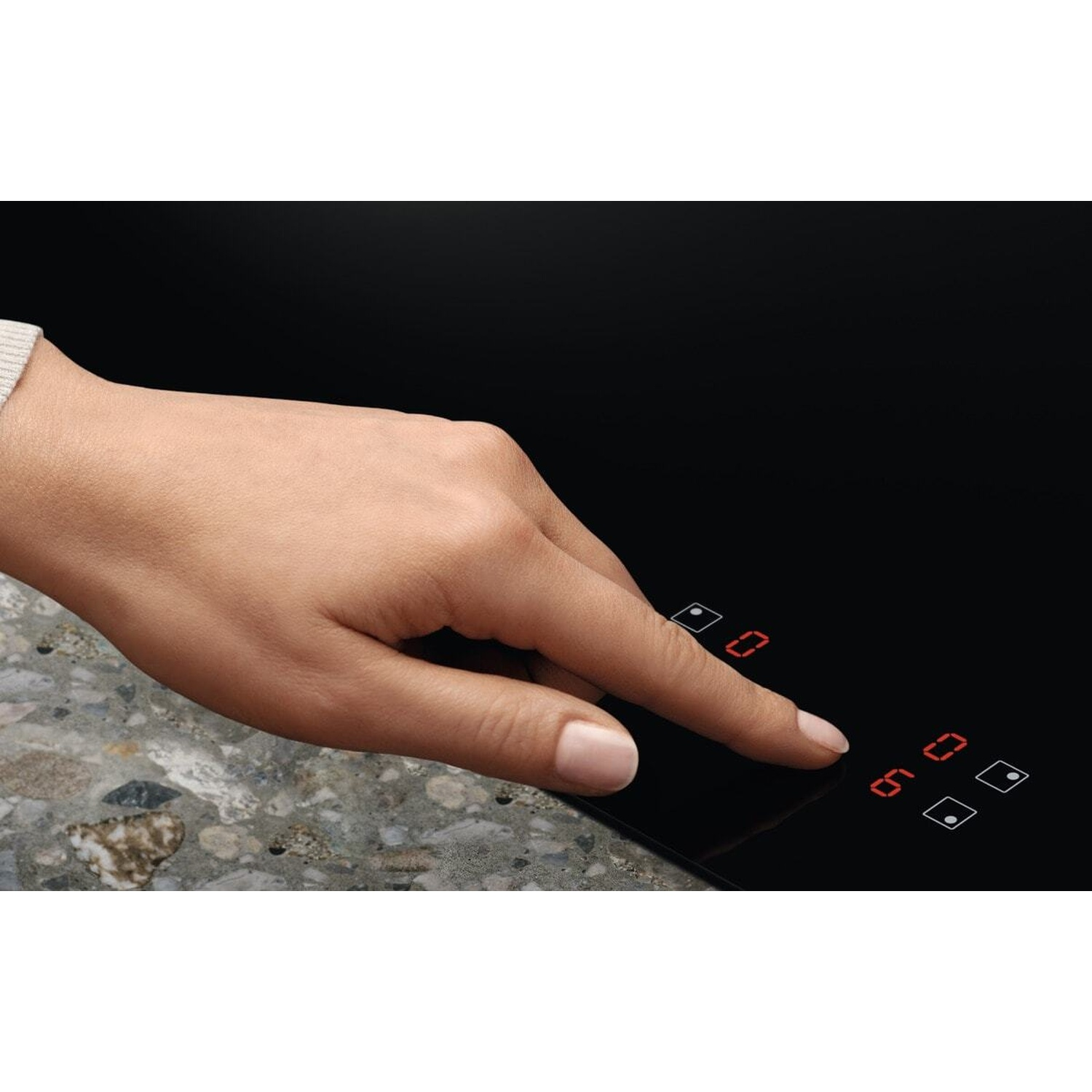 Una mano tocca il touchpad di un piano cottura nero con display digitali rossi.