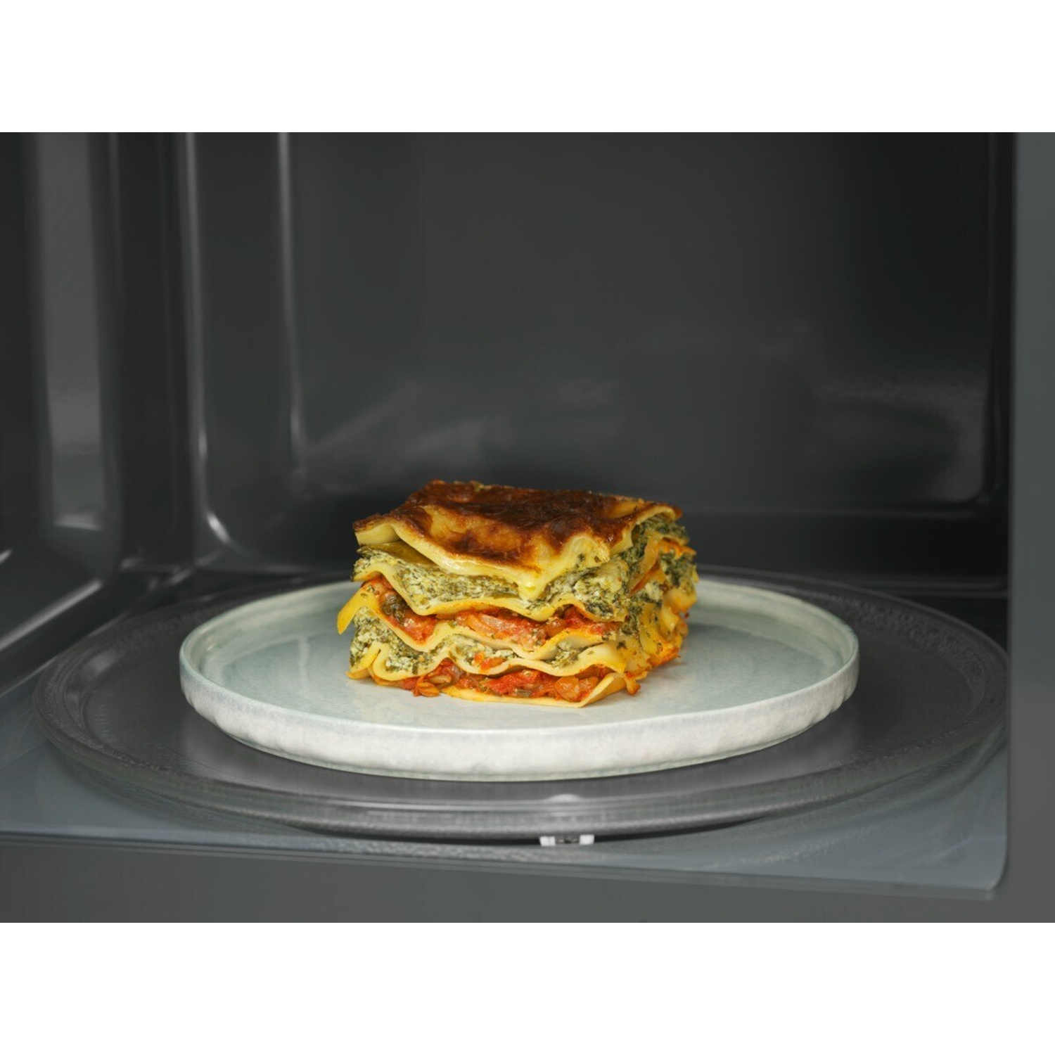 Una porzione impilata di lasagne su un piatto all'interno di un forno a microonde.