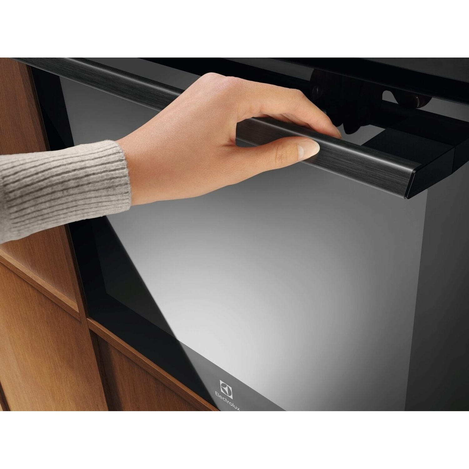 Una mano apre lo sportello di un forno moderno con maniglia in metallo spazzolato.