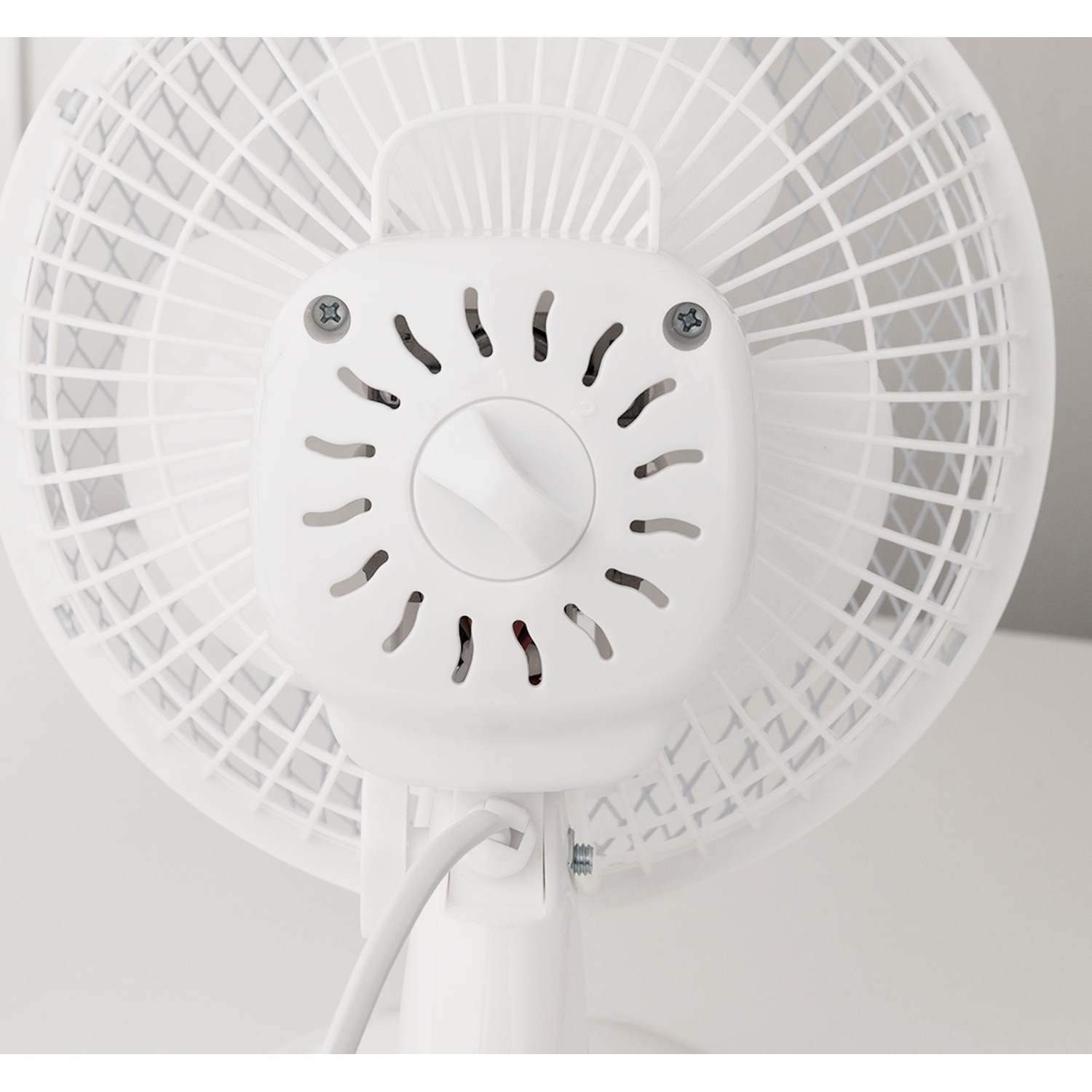 Back of a white fan with protective grille and cable.