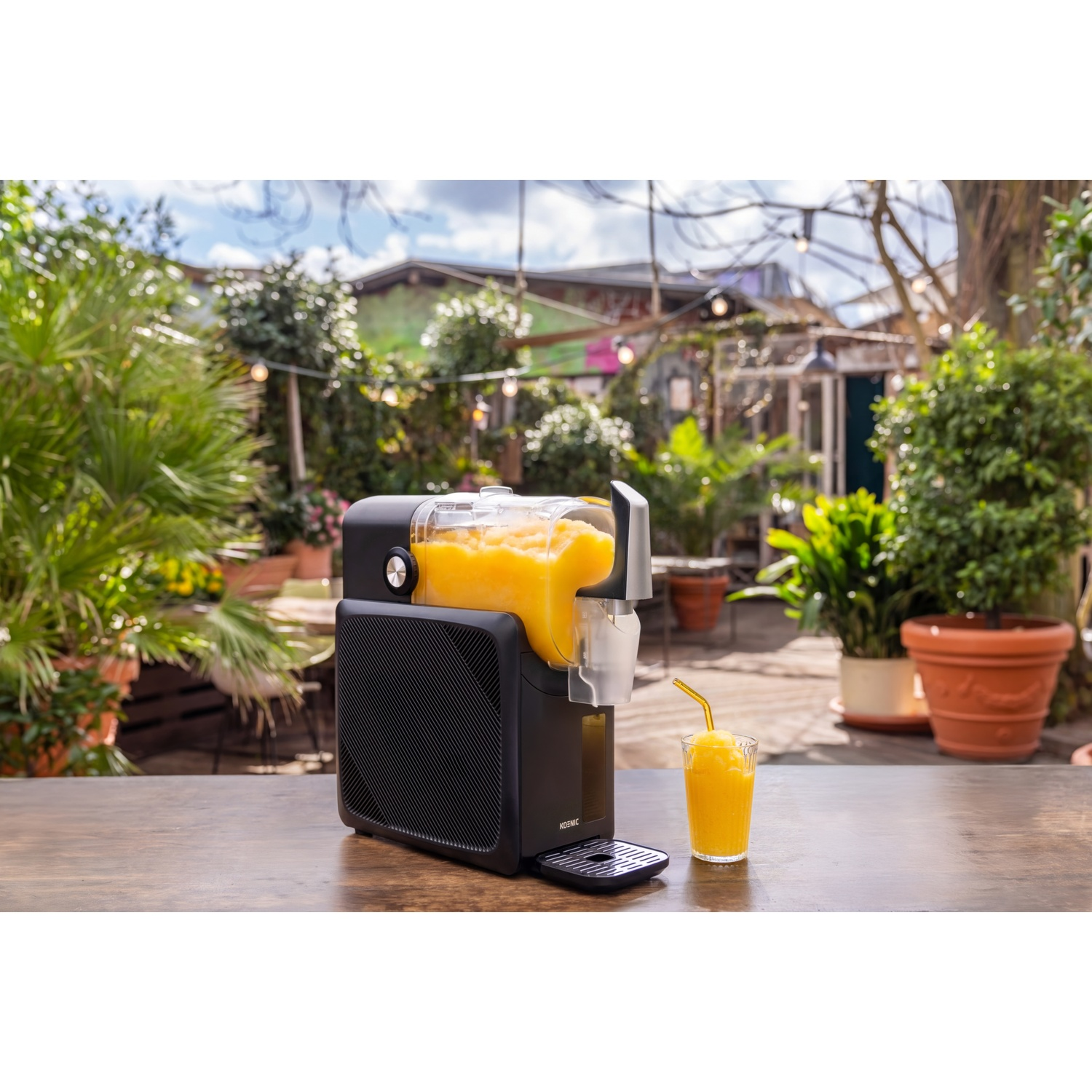 A black juicer with yellow juice, next to it a glass of frozen juice with a straw.