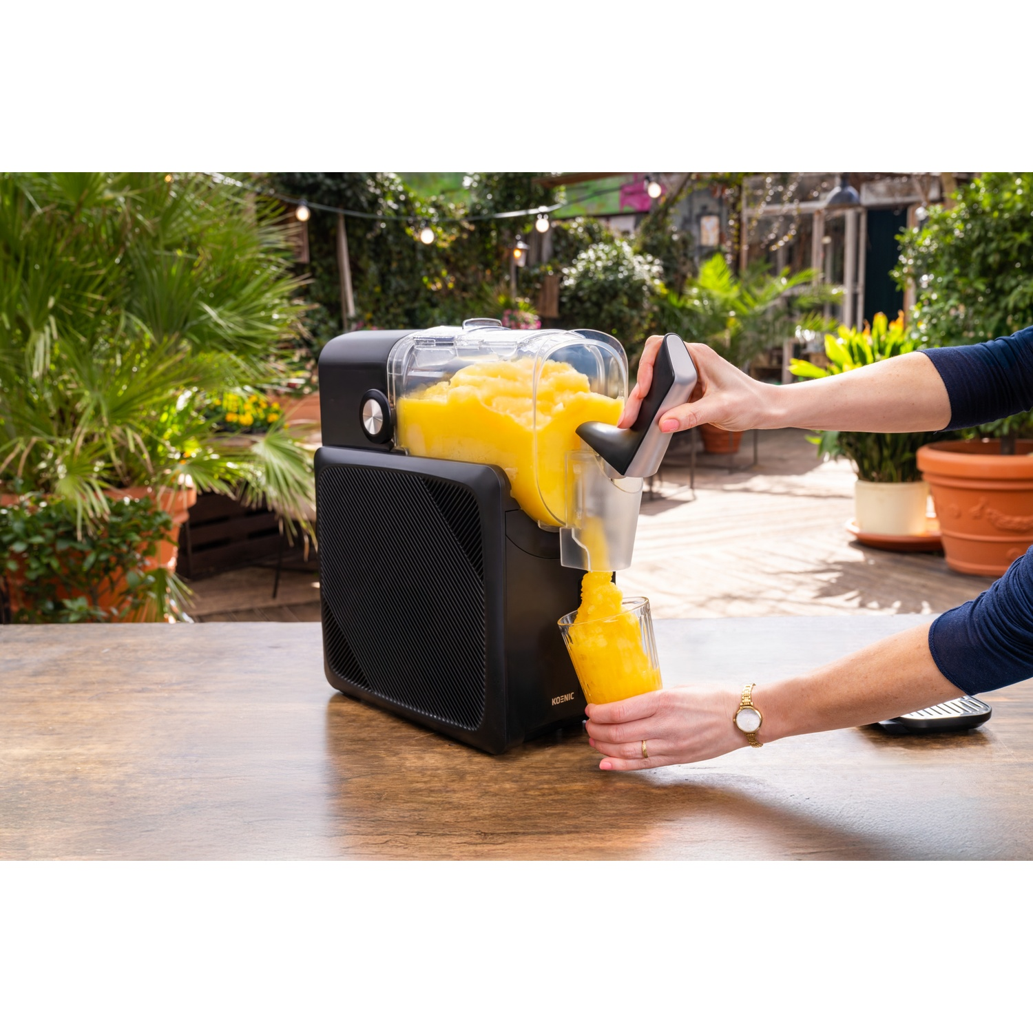 A person dispenses yellow slushy from a machine into a glass outdoors.