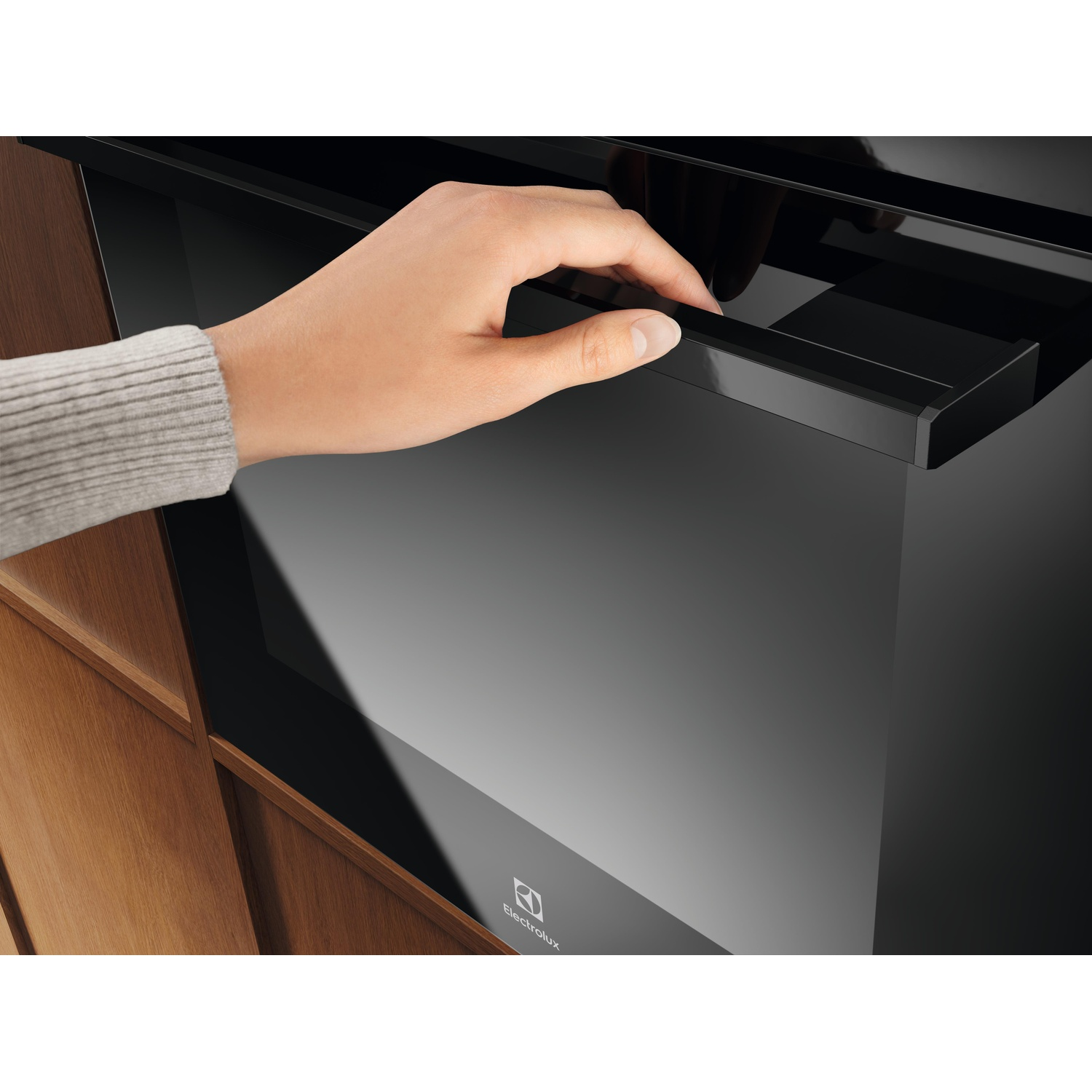 Una mano apre il cassetto di un forno nero accanto a mobili in legno.