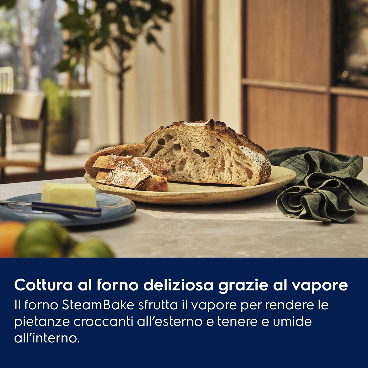 Pane affettato su piatto con burro e tovagliolo verde, stanza luminosa sullo sfondo.
