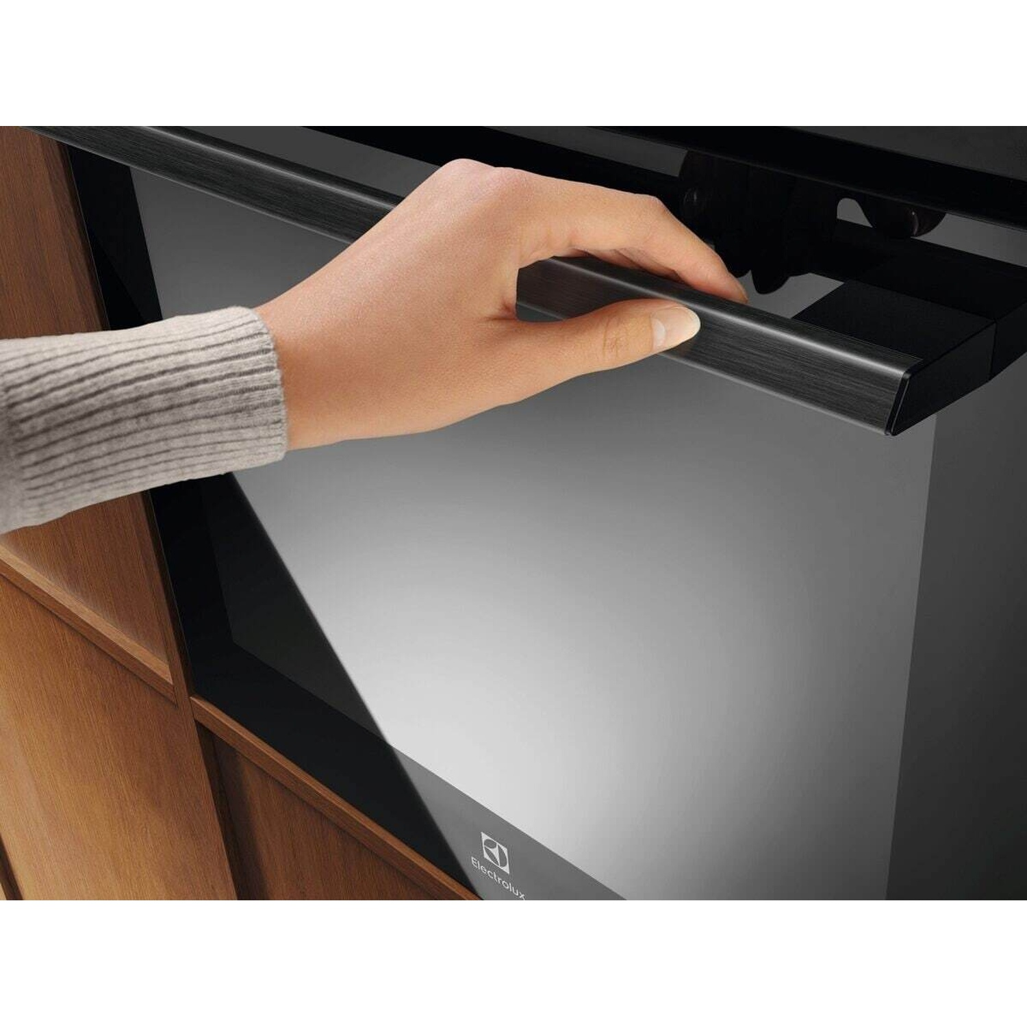 Una mano apre la porta nera di un forno moderno con maniglia spazzolata.