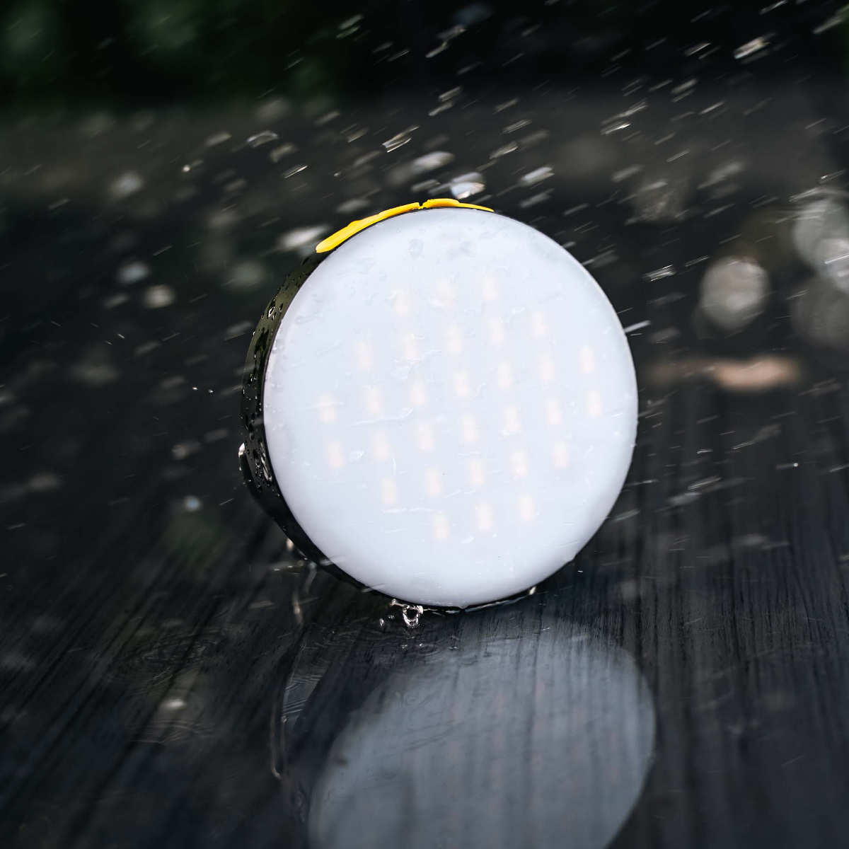 Runde Lampe mit LEDs auf nassem Holztisch, Regentropfen fallen.