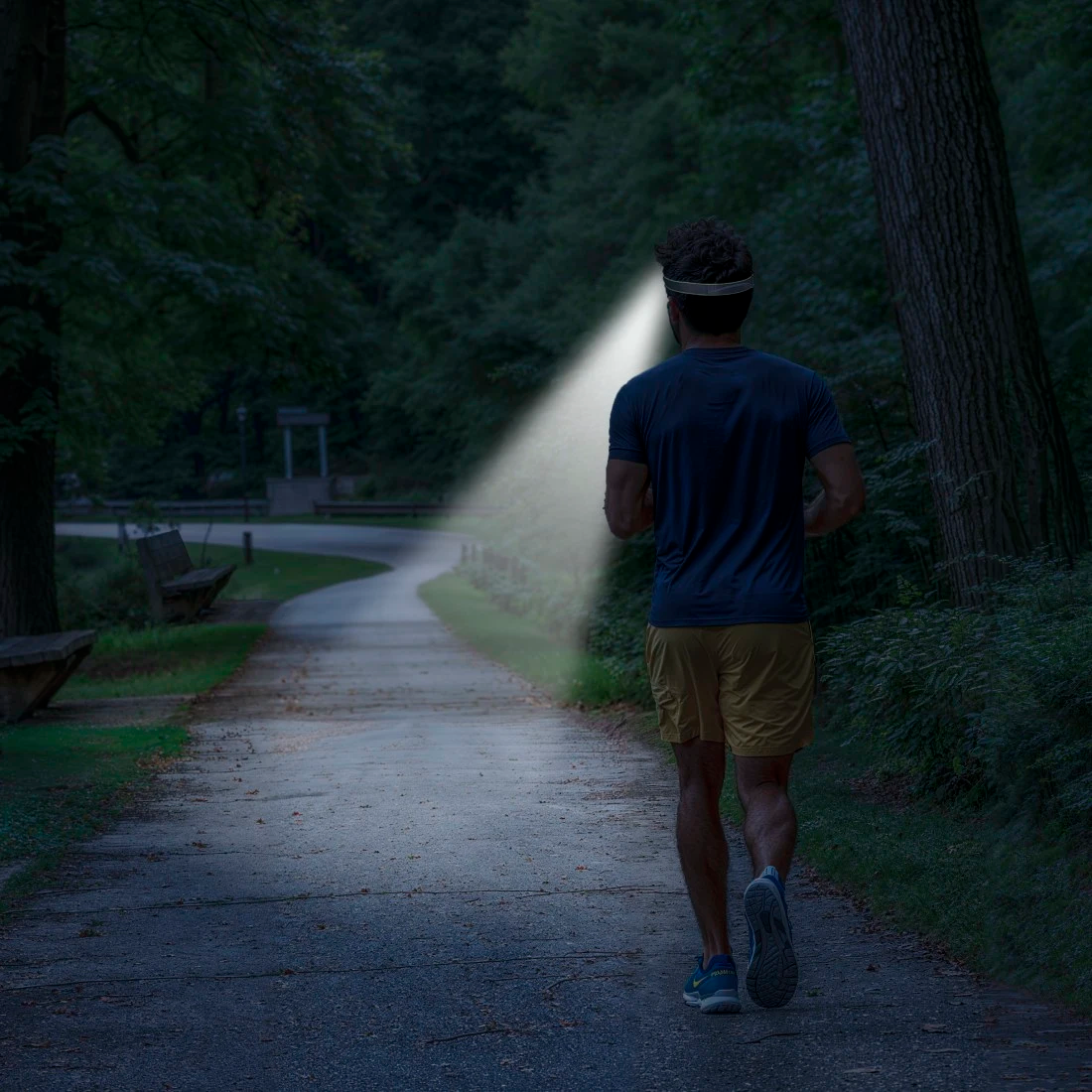 Mann mit Stirnlampe joggt nachts auf einem Waldweg.