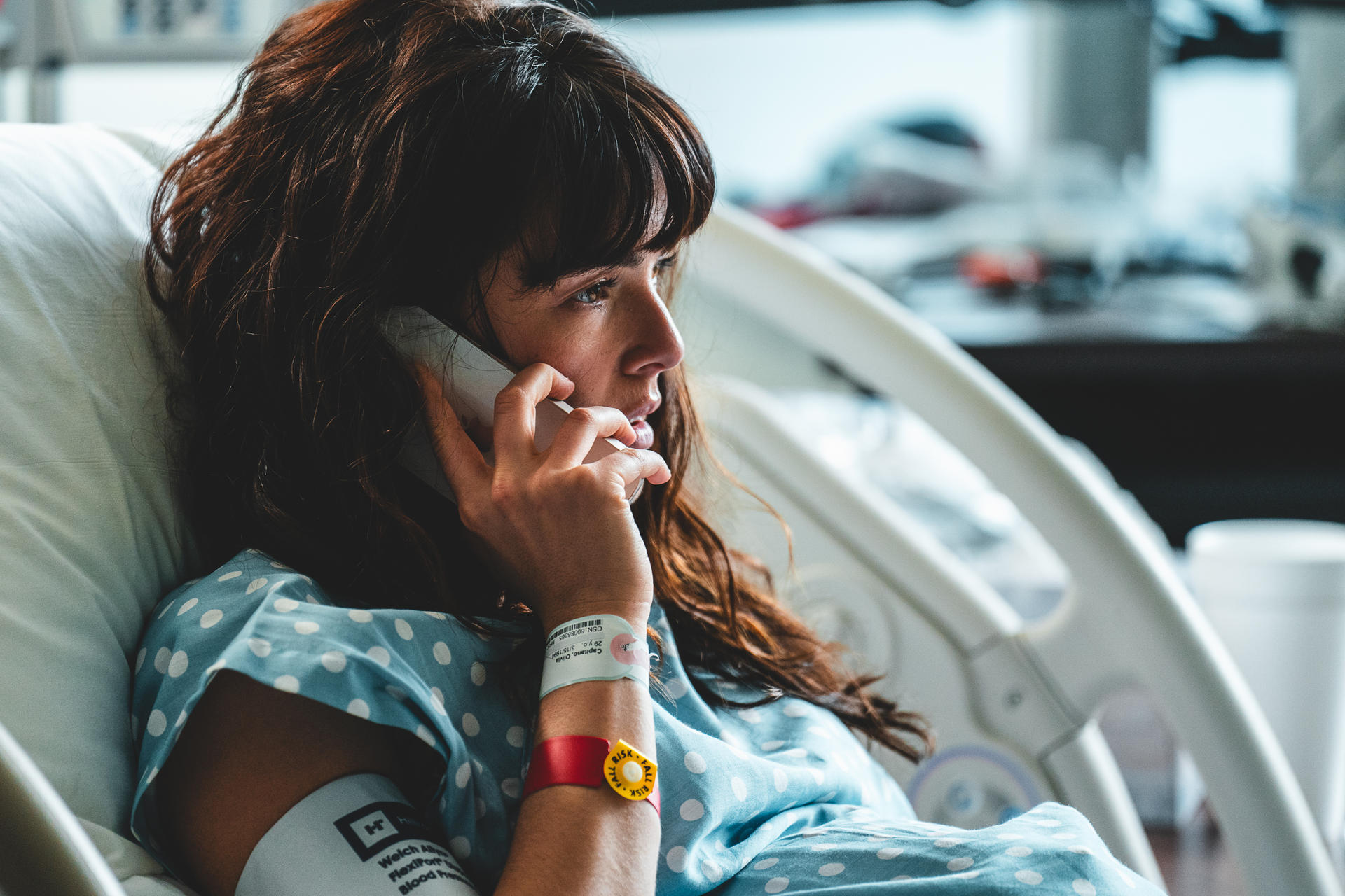 Eine Frau mit dunklem Haar liegt in einem Krankenhausbett und telefoniert.