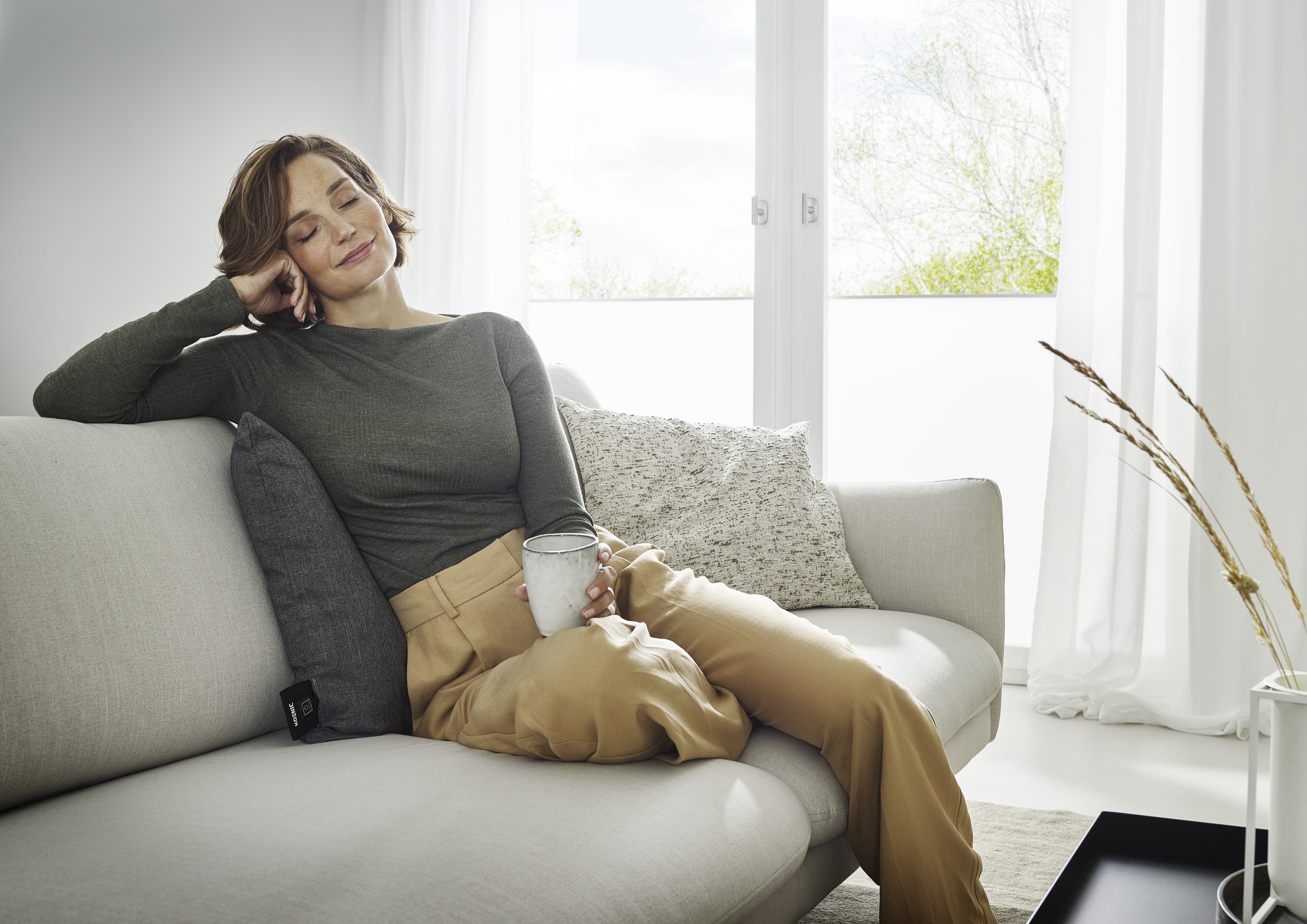 Eine Frau entspannt sich auf einem Sofa mit einer Tasse in der Hand.