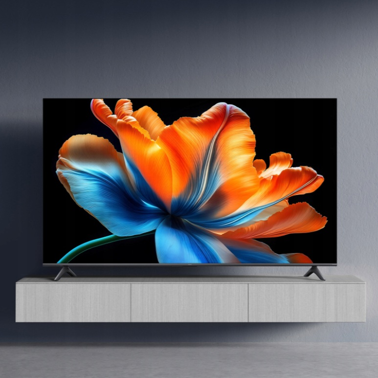 Duży telewizor wyświetla jaskrawo pomarańczowo-niebieski kwiat na czarnym tle, na szarym stojaku.