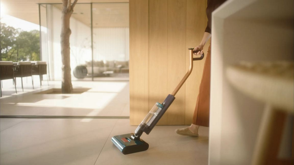 Une personne nettoie le sol avec un aspirateur balai sans fil dans une maison moderne.