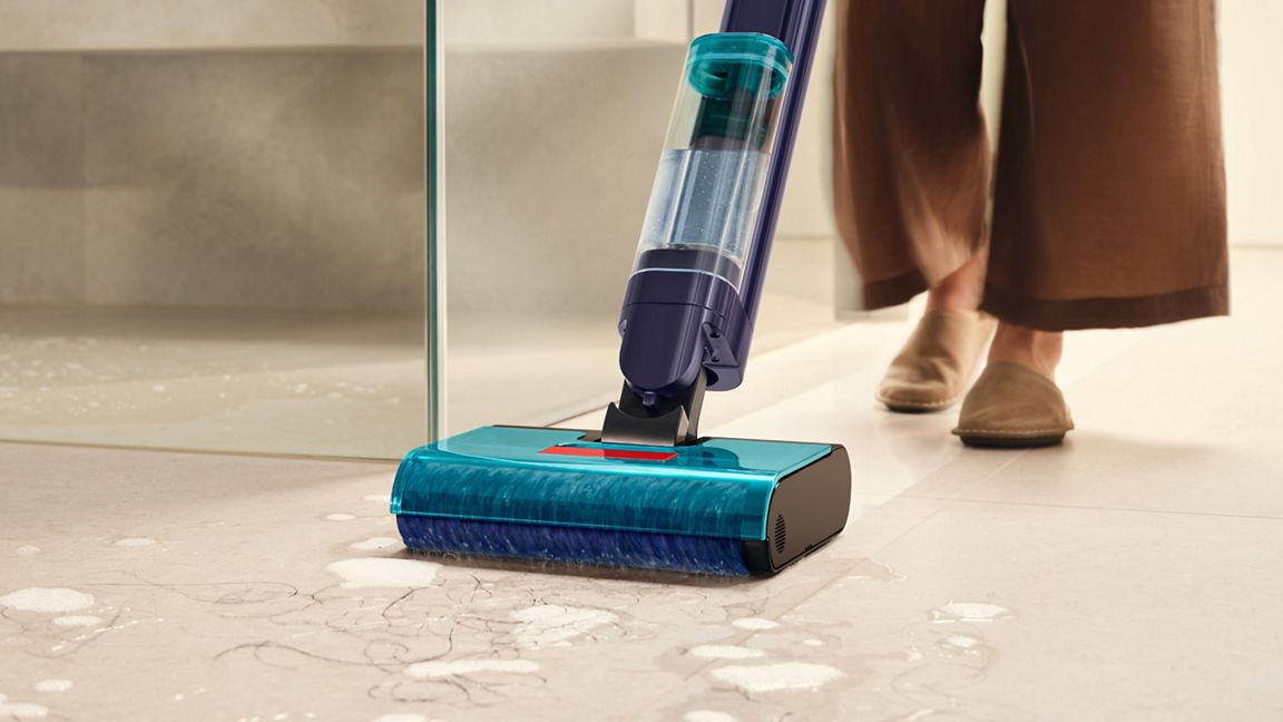 Un aspirateur eau et poussière bleu nettoie un sol carrelé avec de l'eau et des cheveux.
