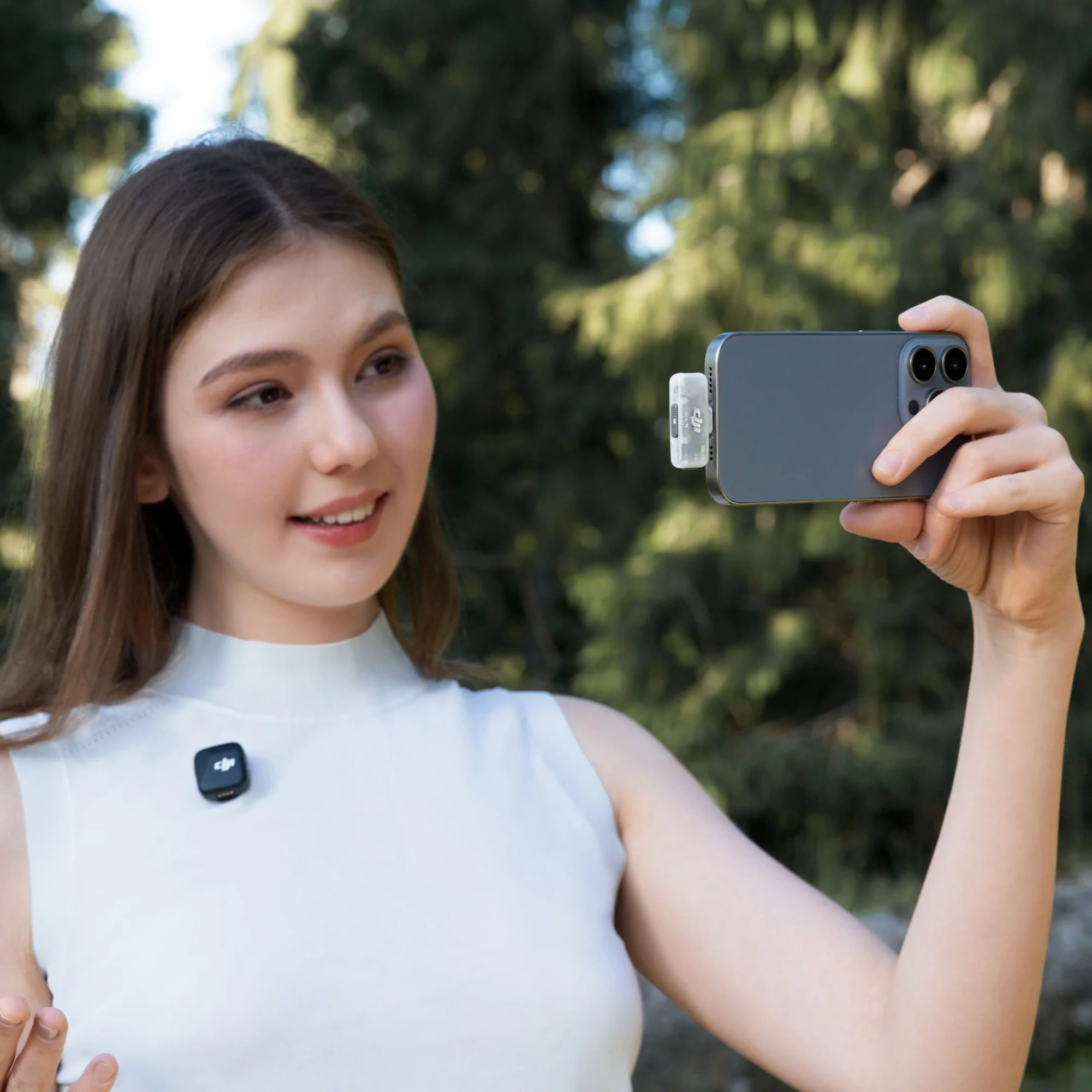 Une jeune femme tient un smartphone pour prendre un selfie. Un microphone est attaché.