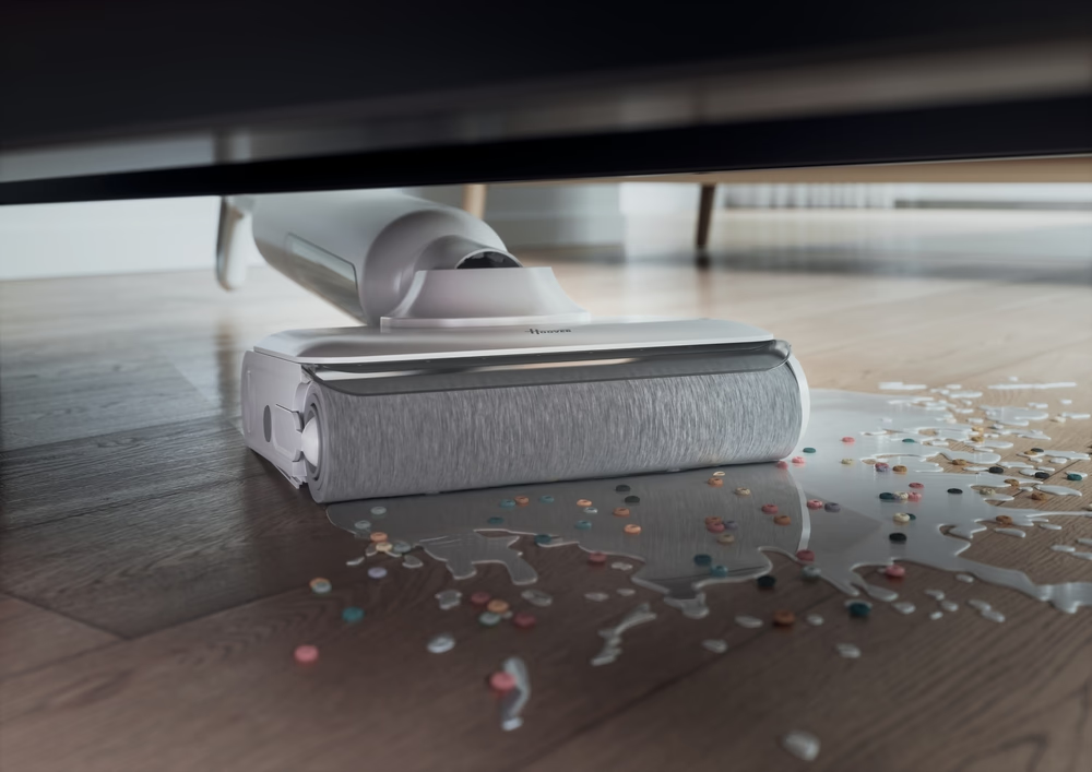 Ein weißer Bodenreiniger reinigt verschüttete Flüssigkeit und kleine bunte Konfetti auf Holzboden.