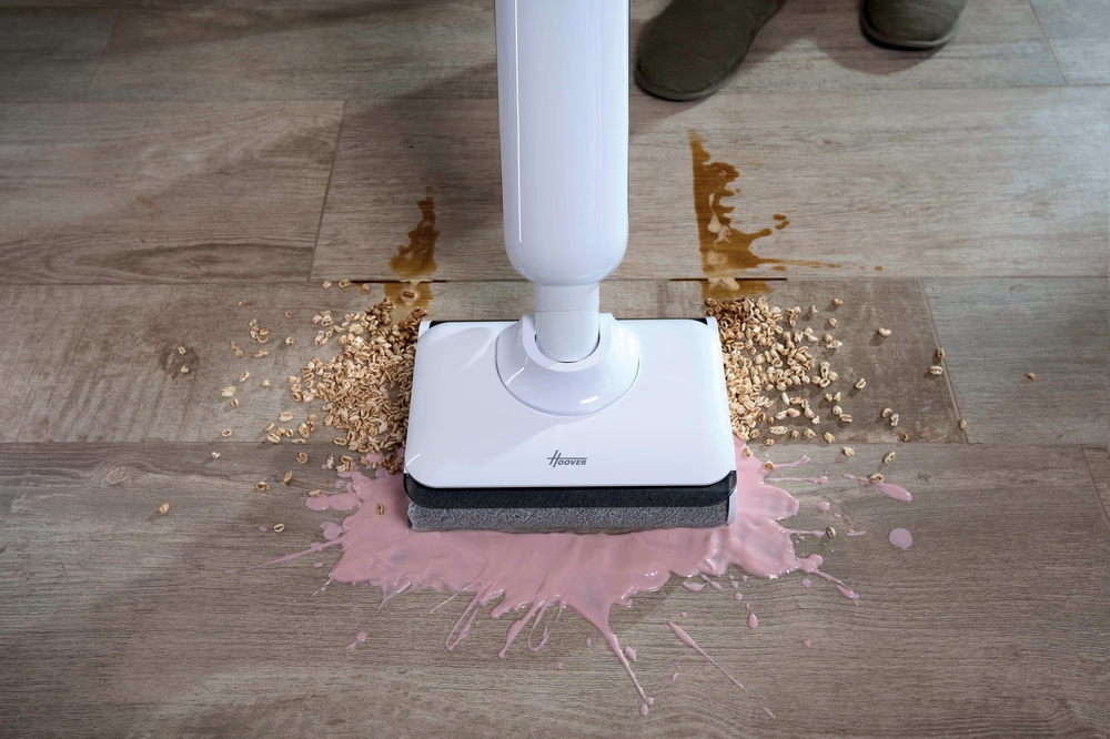 Ein weißer Bodenwischer reinigt verschüttete Milch und Müsli auf Holzboden.