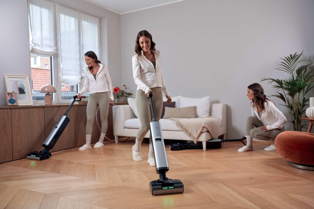 Drei Frauen reinigen einen Holzboden mit einem Nasswischer.