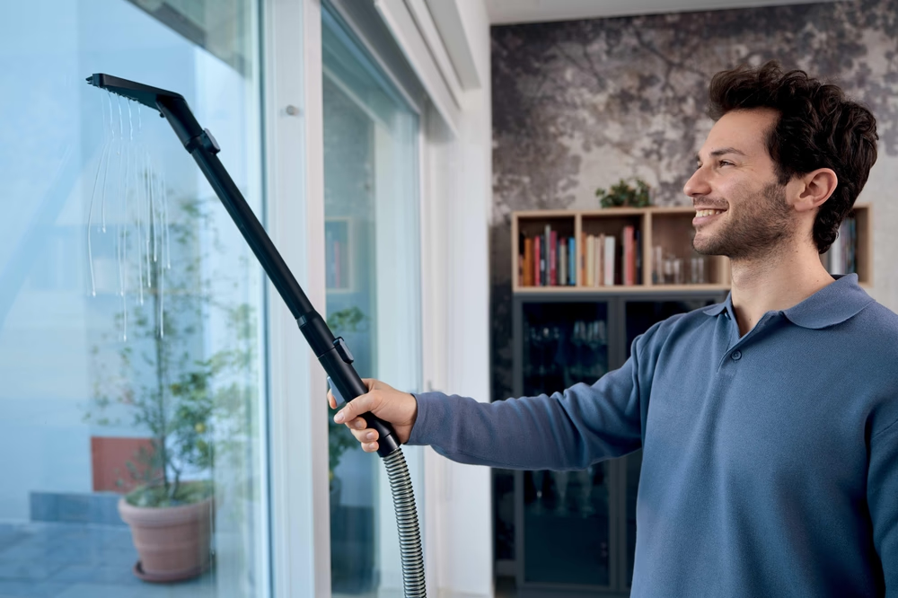 Ein Mann reinigt ein Fenster mit einem Dampfreiniger, der Wasser sprüht.