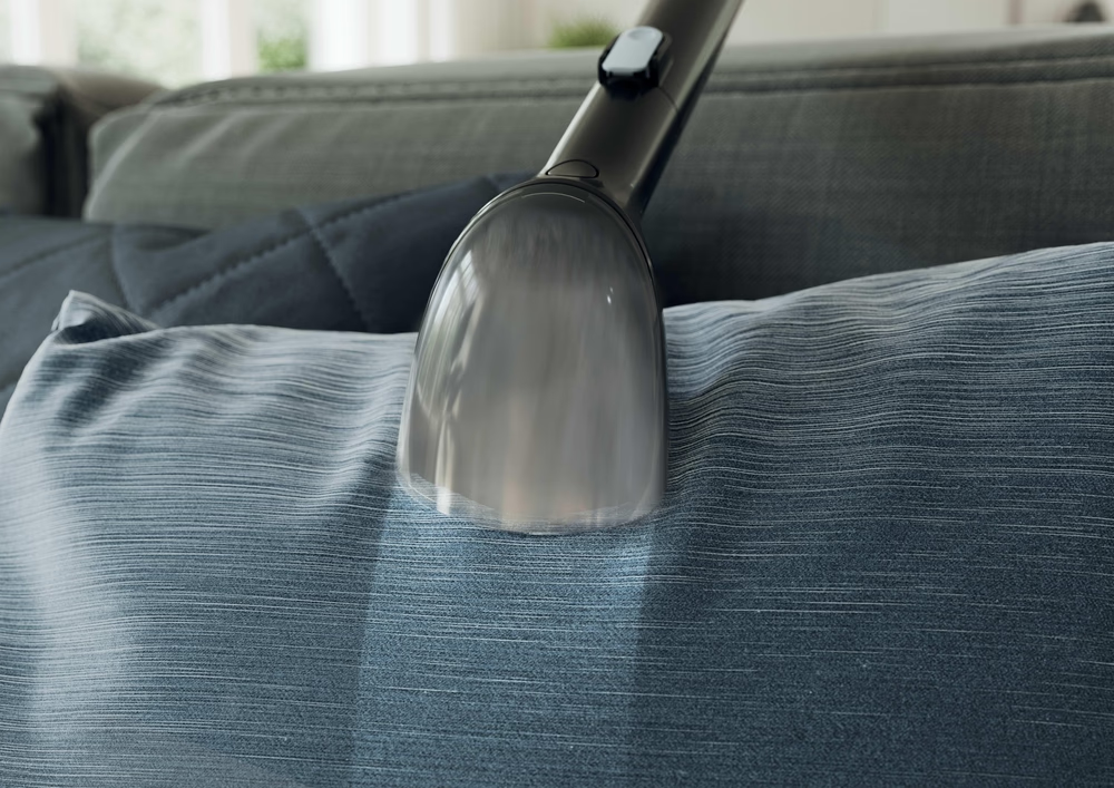 Ein Staubsaugeraufsatz reinigt ein blaues Kissen auf einem Sofa.