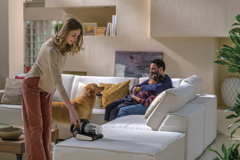 Frau mit Staubsauger, Hund und Familie auf Sofa im Wohnzimmer.