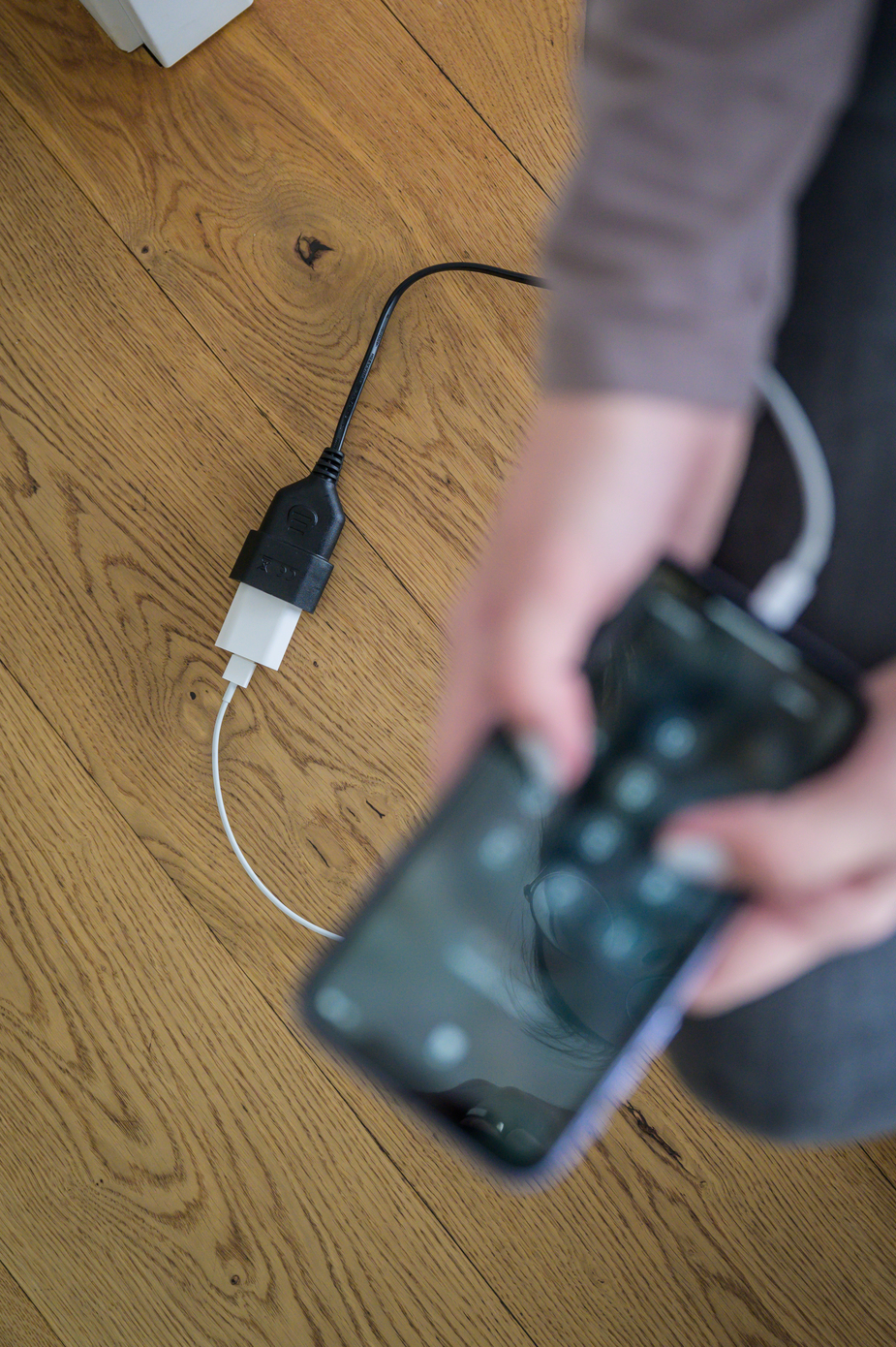 Eine Person steckt ein Smartphone in eine Steckdose an einem Holzboden.