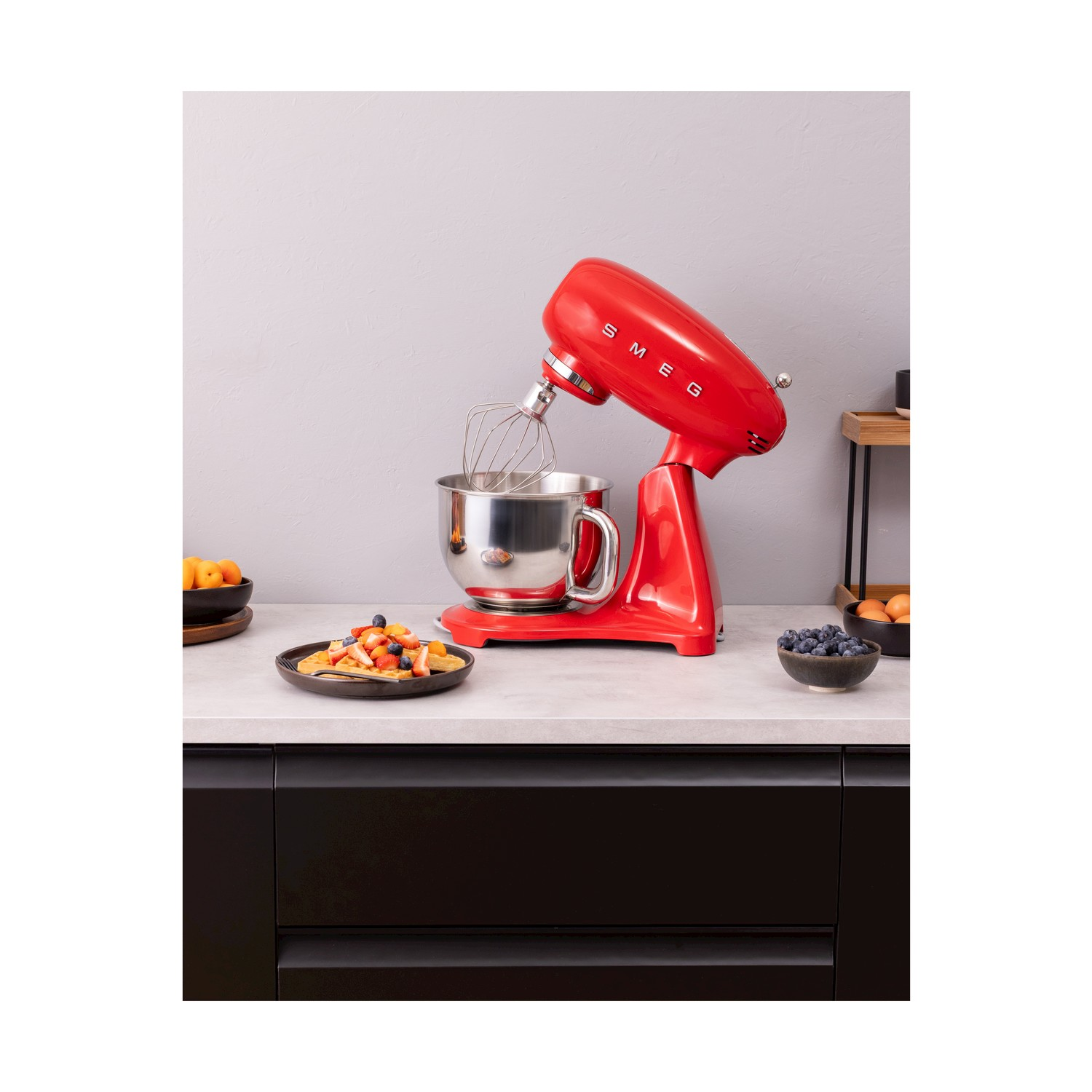 Impastatrice rossa SMEG con una ciotola di frutta e mirtilli su un bancone.
