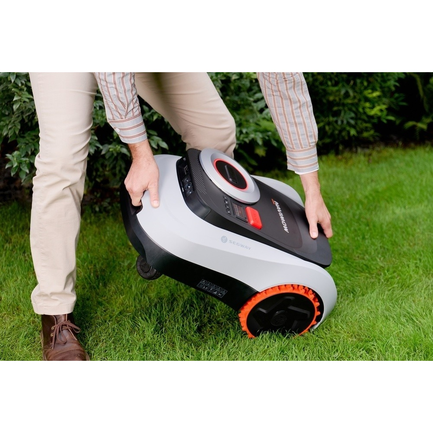 Uomo che tiene un robot tosaerba con ruote arancioni sull'erba.