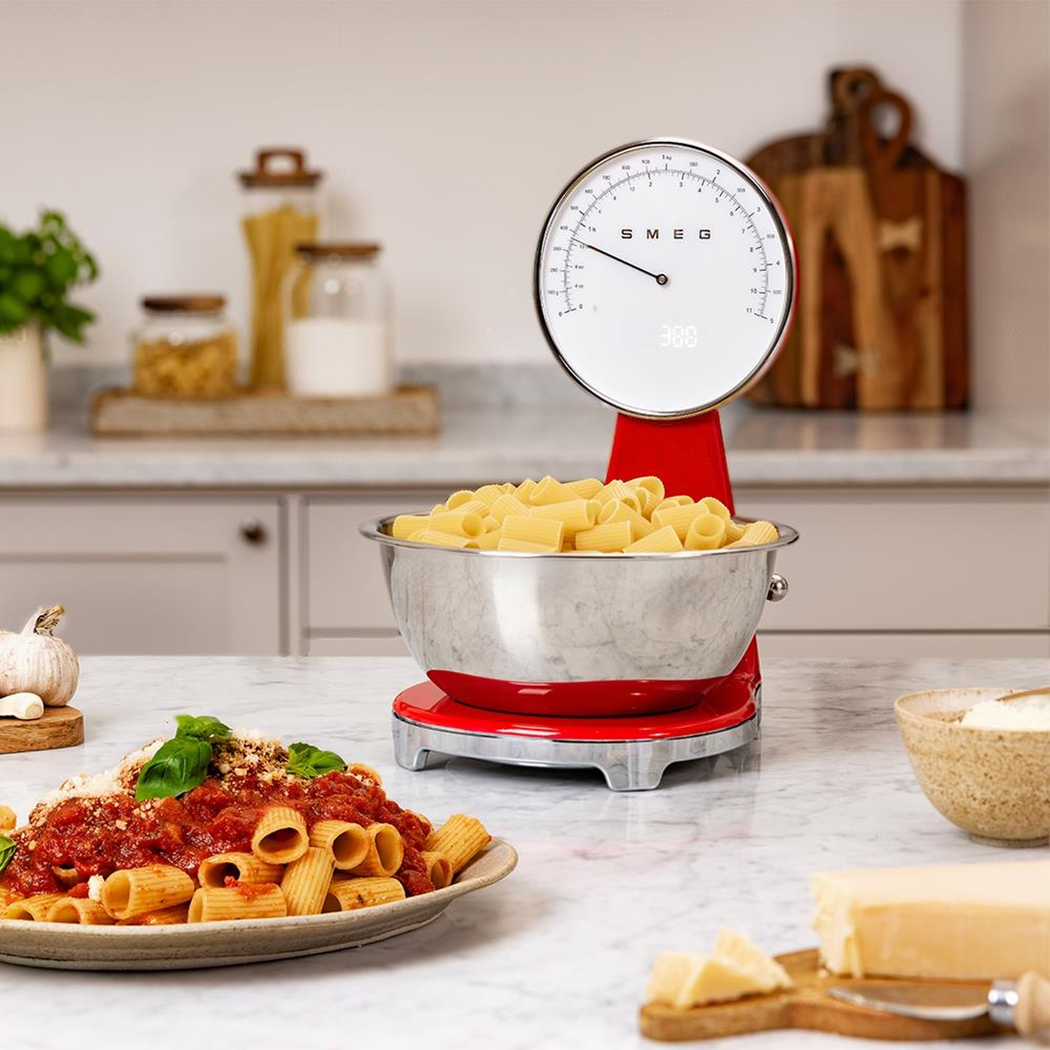 Bilancia da cucina rossa con ciotola di pasta, piatto di pasta e formaggio.