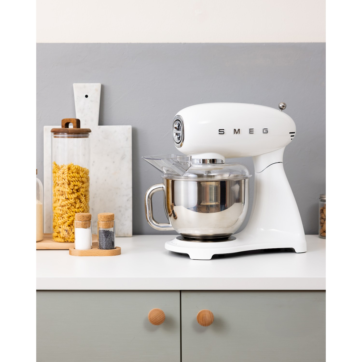 Un'impastatrice Smeg bianca su un piano di lavoro con pasta e spezie.