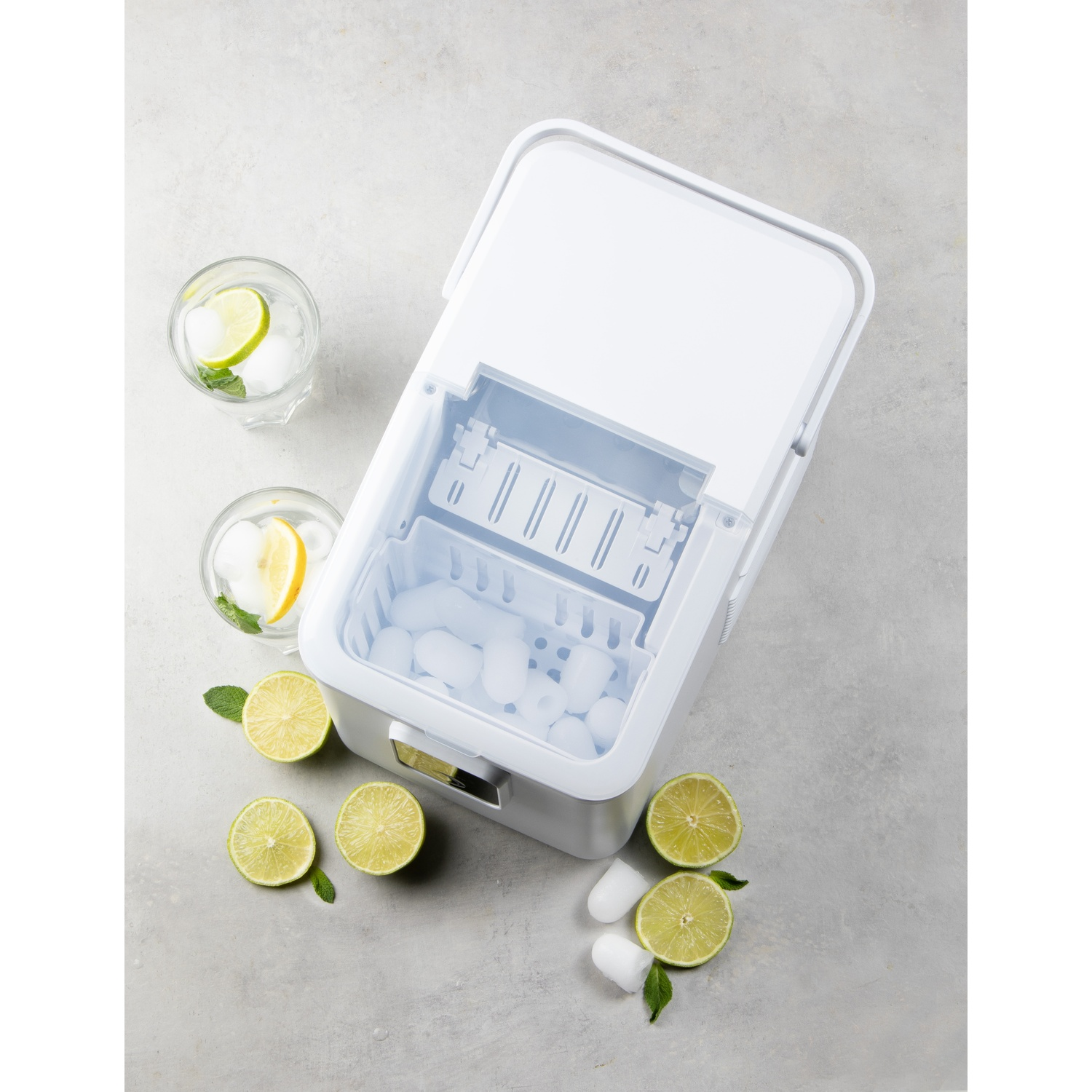 Une machine à glaçons blanche avec des glaçons et des verres avec des tranches de citron et de lime.